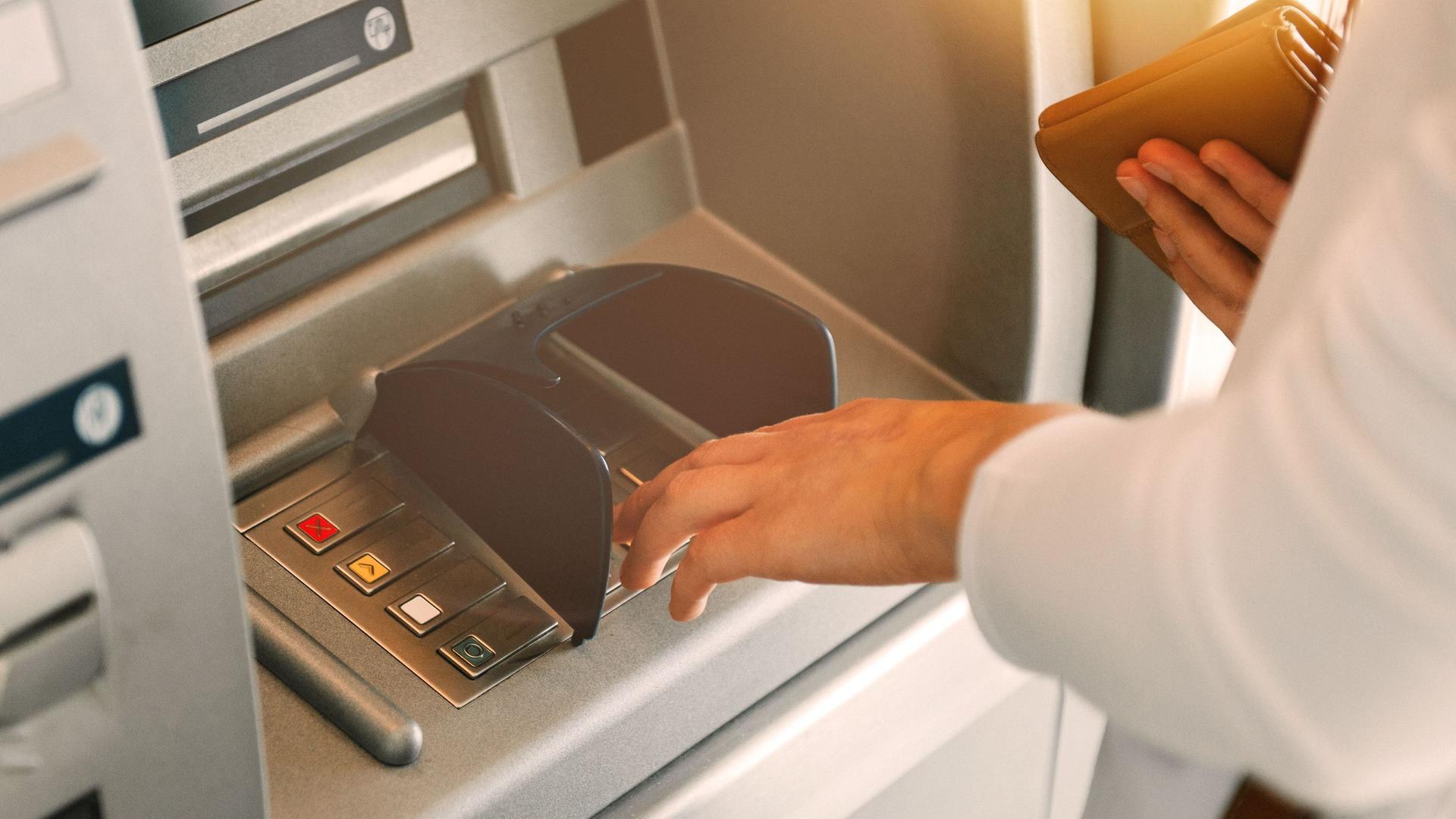 Nahaufnahme einer Frau, die den Pin-Code am Bankautomaten eingibt.