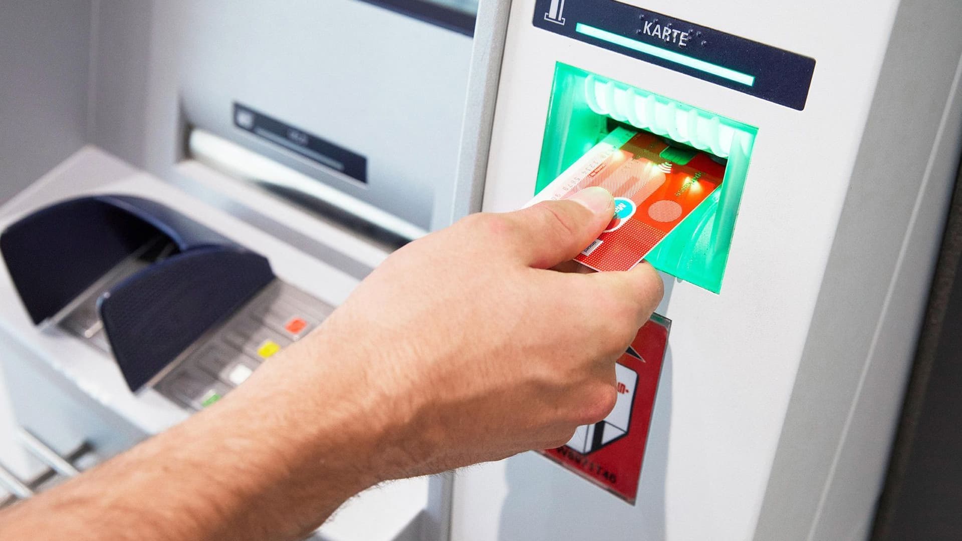 Nahaufnahme einer männlichen Hand, die einer Sparkassenbankkarte in einen Bankautomaten einführt.