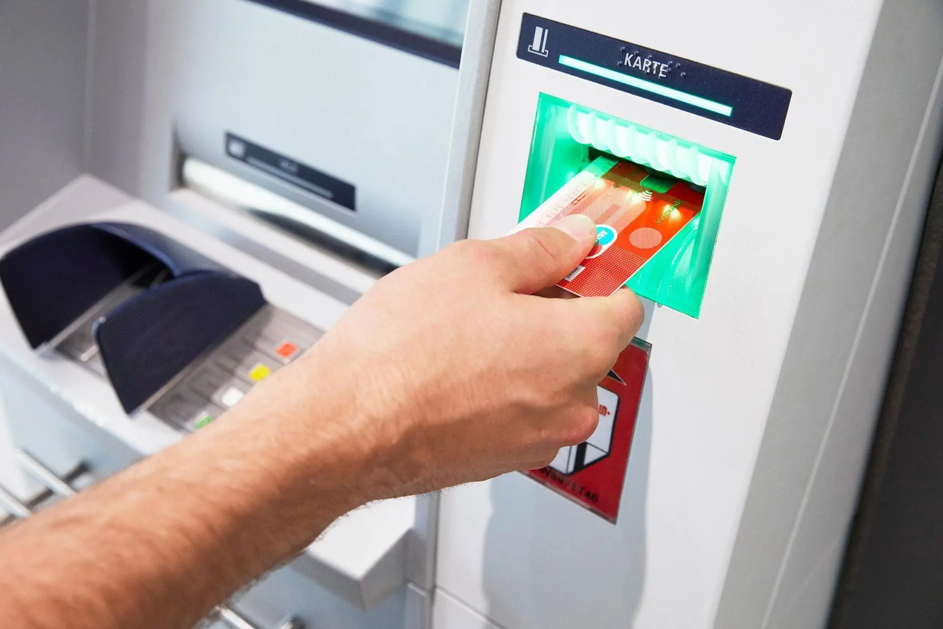 Nahaufnahme einer männlichen Hand, die einer Sparkassenbankkarte in einen Bankautomaten einführt.