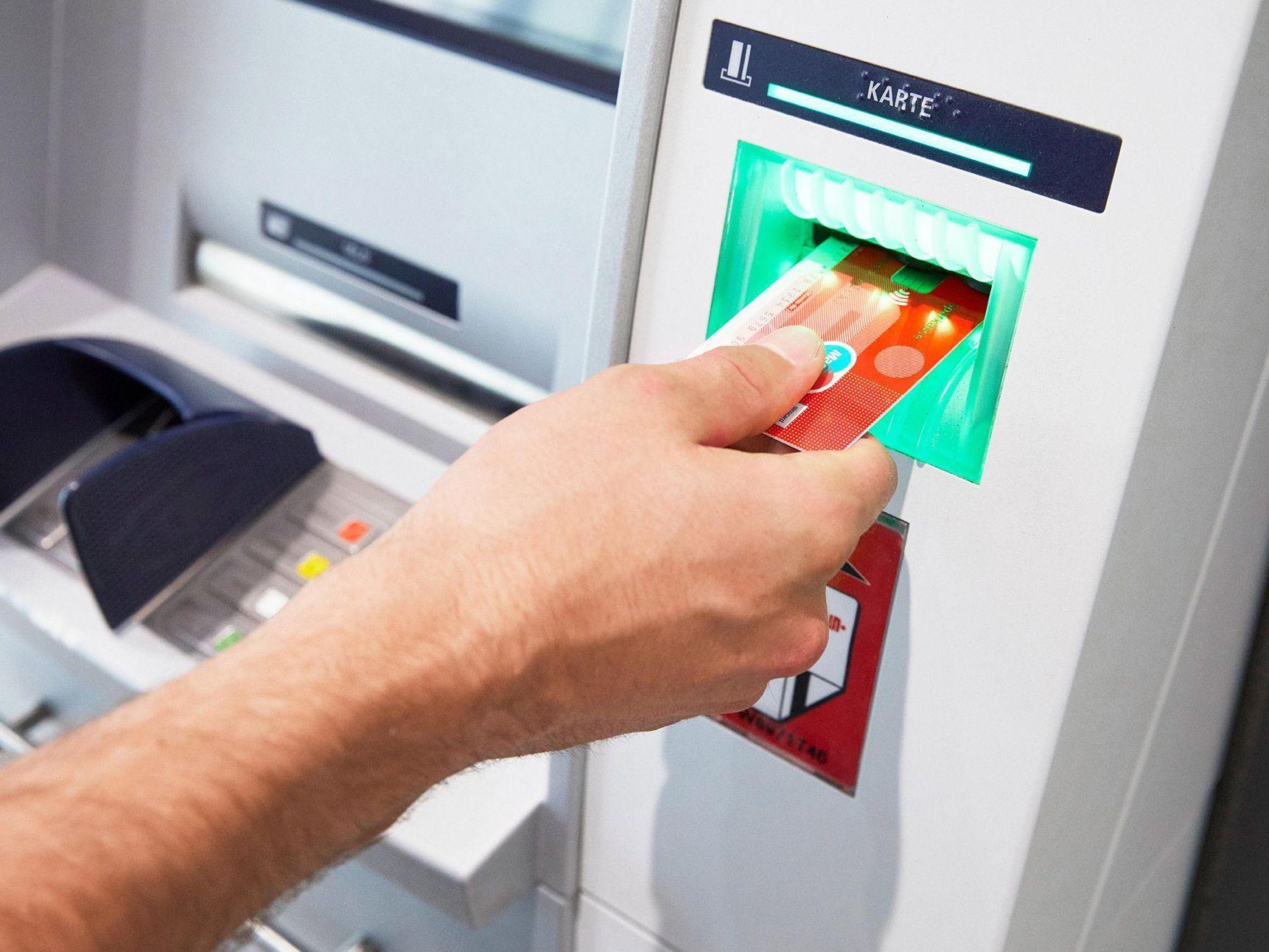 Nahaufnahme einer männlichen Hand, die einer Sparkassenbankkarte in einen Bankautomaten einführt.