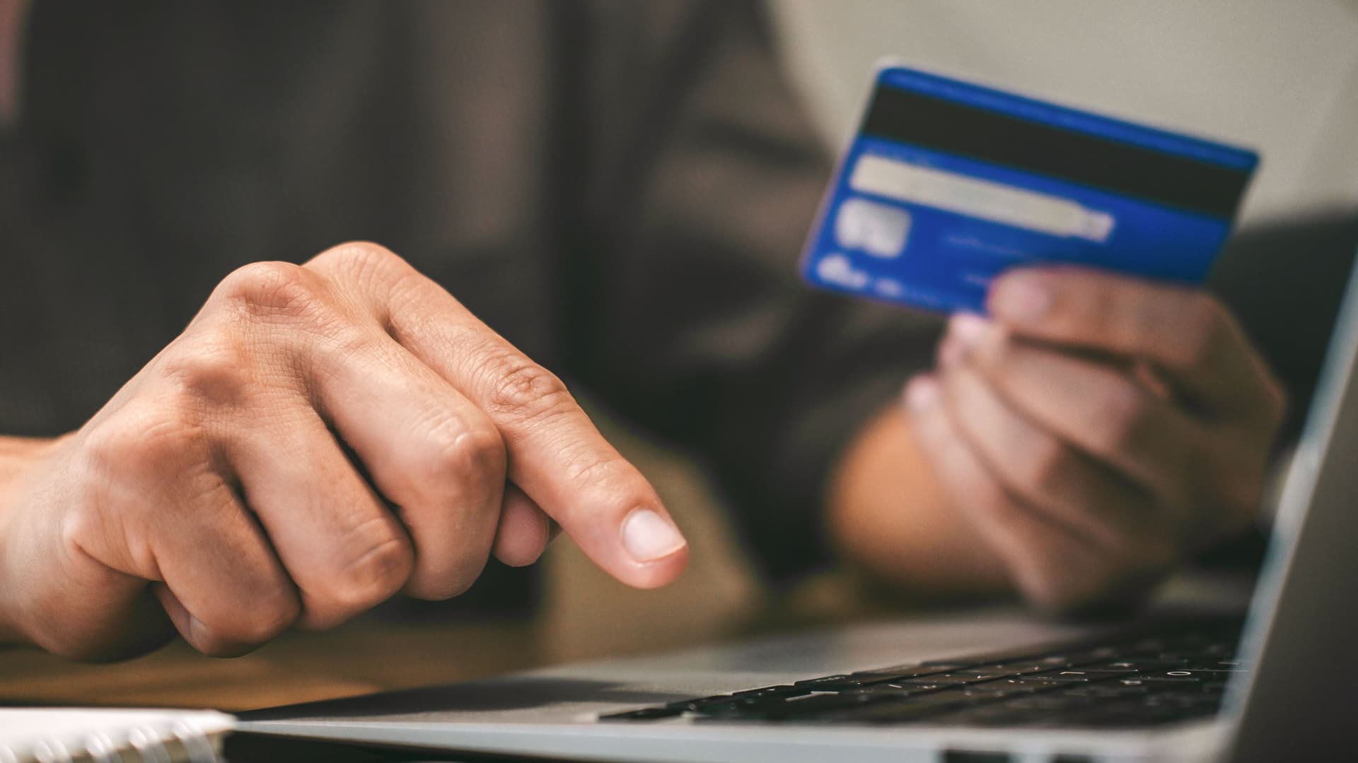 So bezahlen Sie sicher Nahaufnahme einer Person mit Bankkarte in der Hand vor einem Laptop.