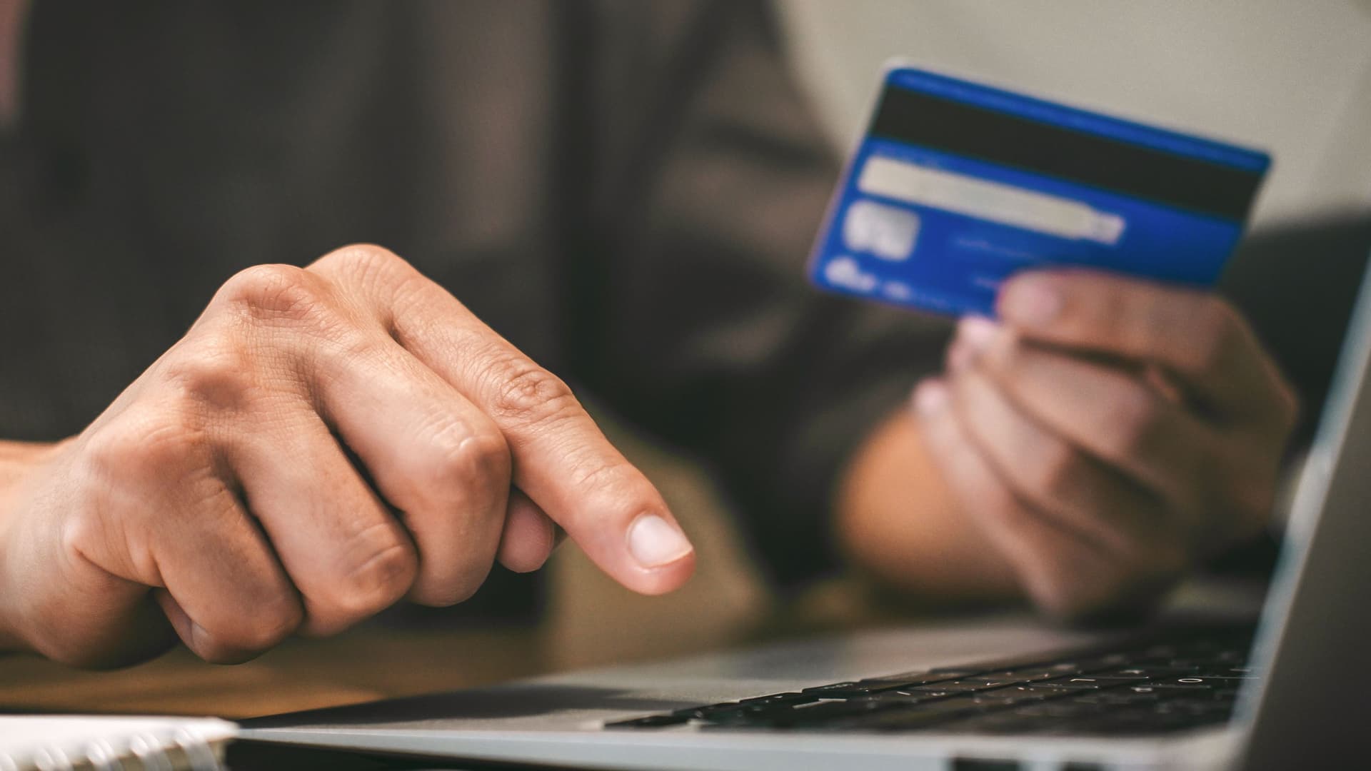 Nahaufnahme einer Person mit Bankkarte in der Hand vor einem Laptop.