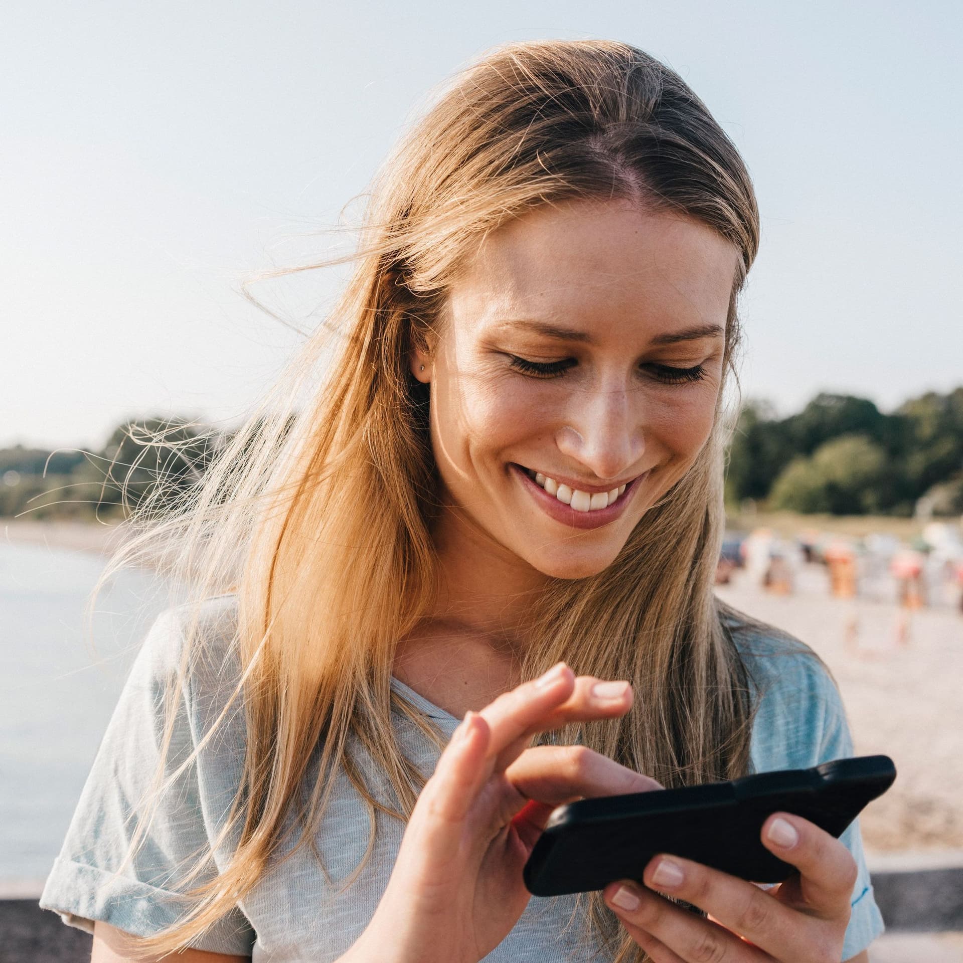 Eine junge Frau steht am Strand und benutzt ihr Smartphone