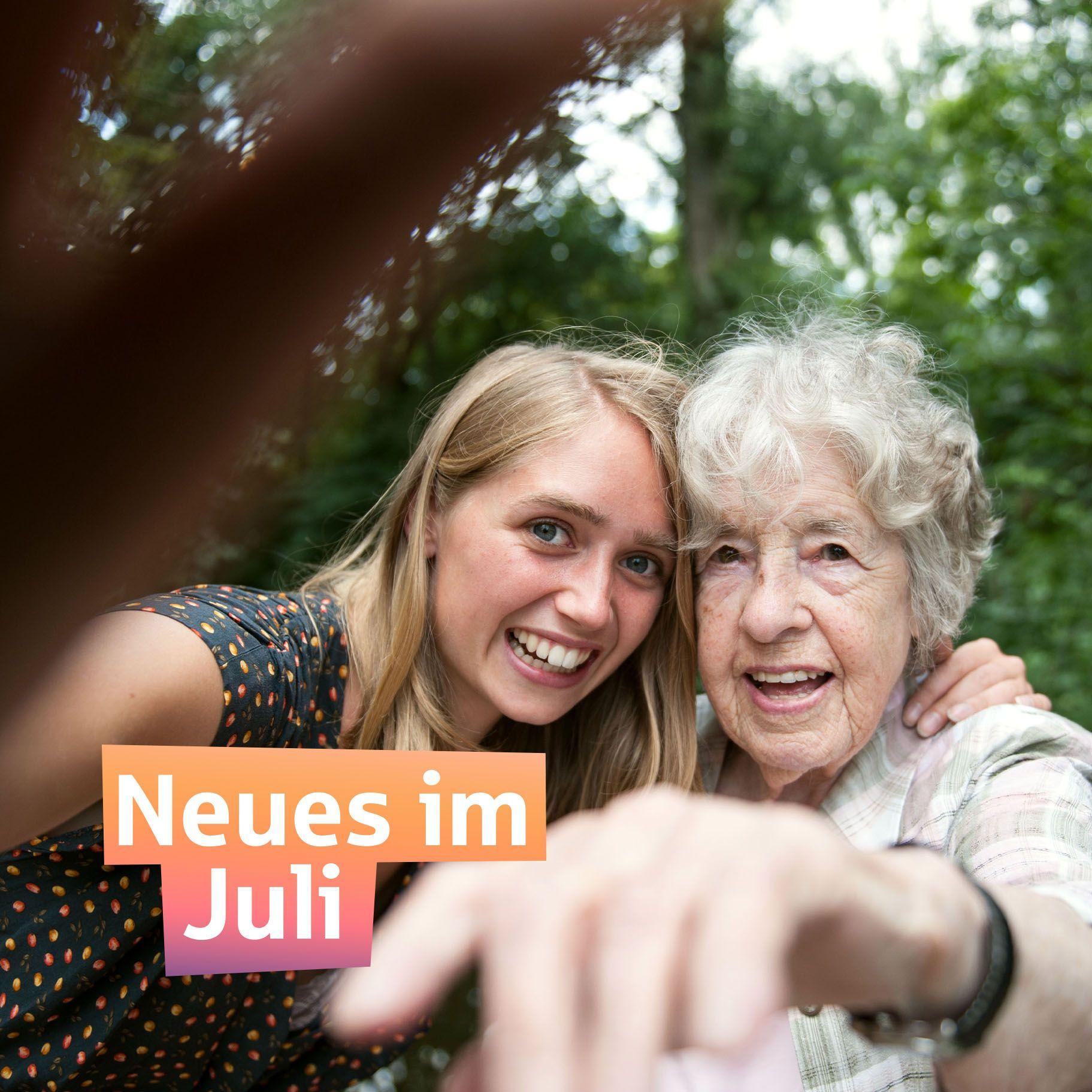 Eine junge Frau macht im Garten ein Selfie mit ihrer Oma. Beide lachen in die Kamera.