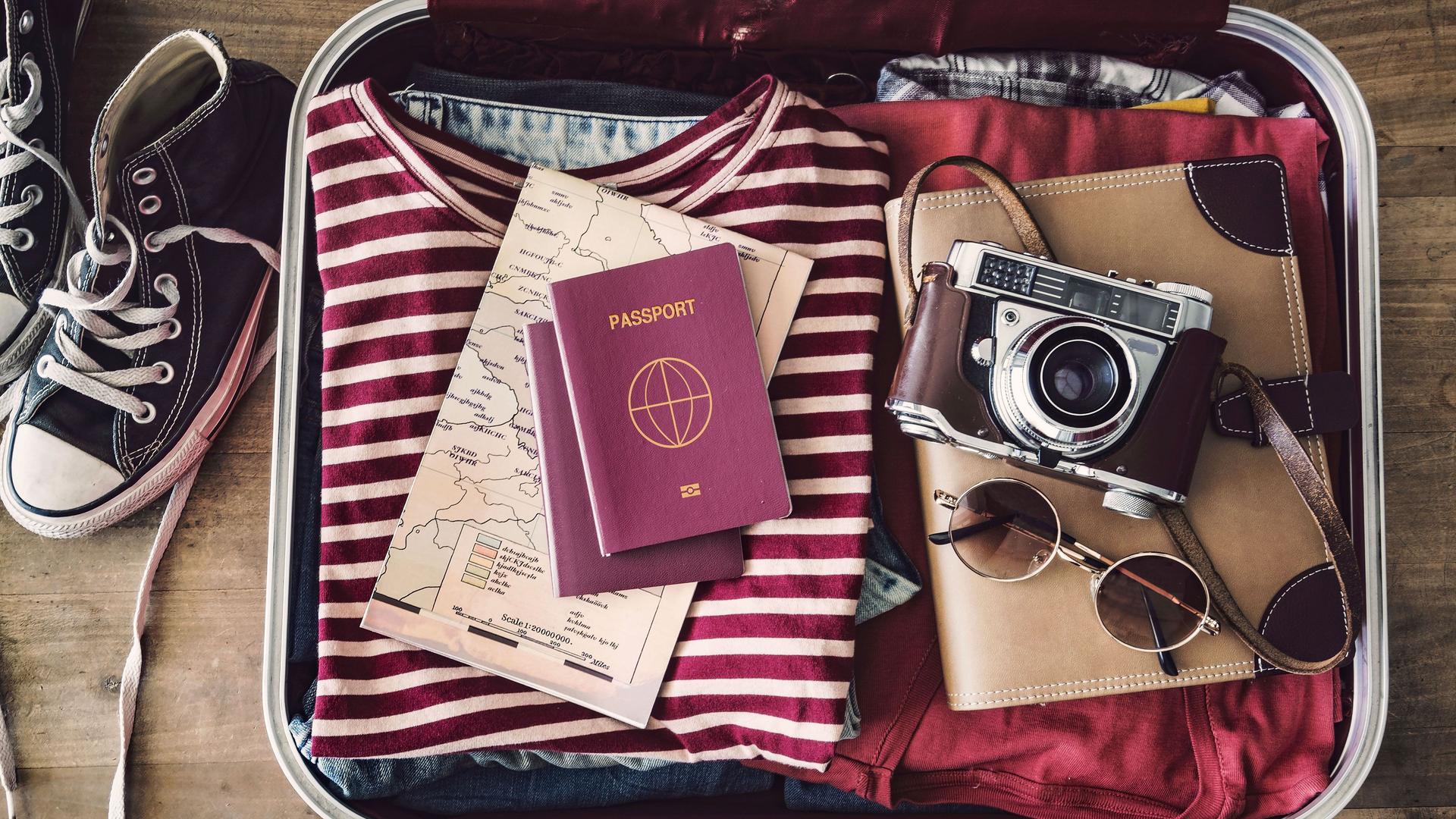 Offener Reisekoffer von oben fotografiert. Neben dem Koffer stehen schwarze Converse Schuhe.