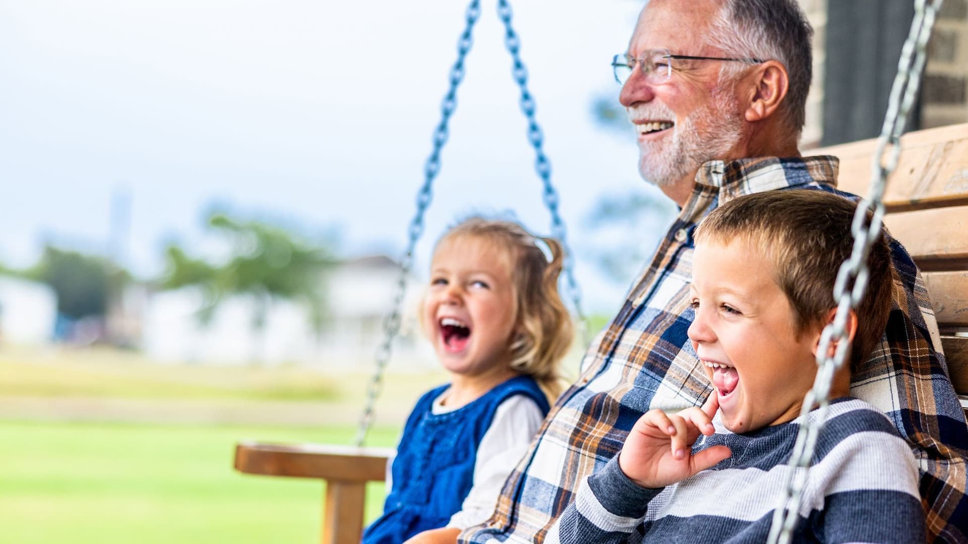 Ein Senior sitzt mit seinen Enkeln auf einer Schaukel und lacht.