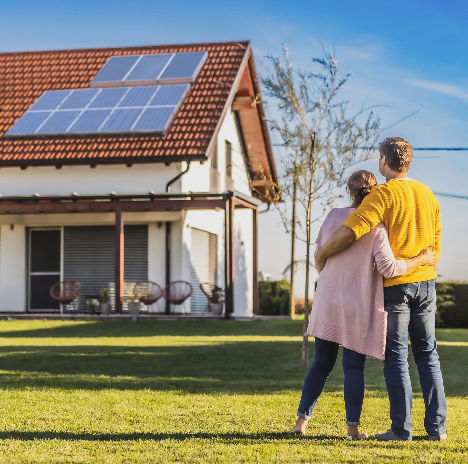 Paar steht umarmt auf dem Rasen vor einem Einfamilienhaus mit Solaranlage