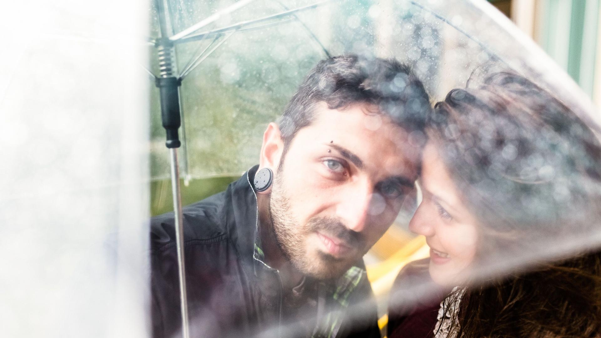 Junges Paar steht unter einem durchsichtigen Regenschirm im Regen.