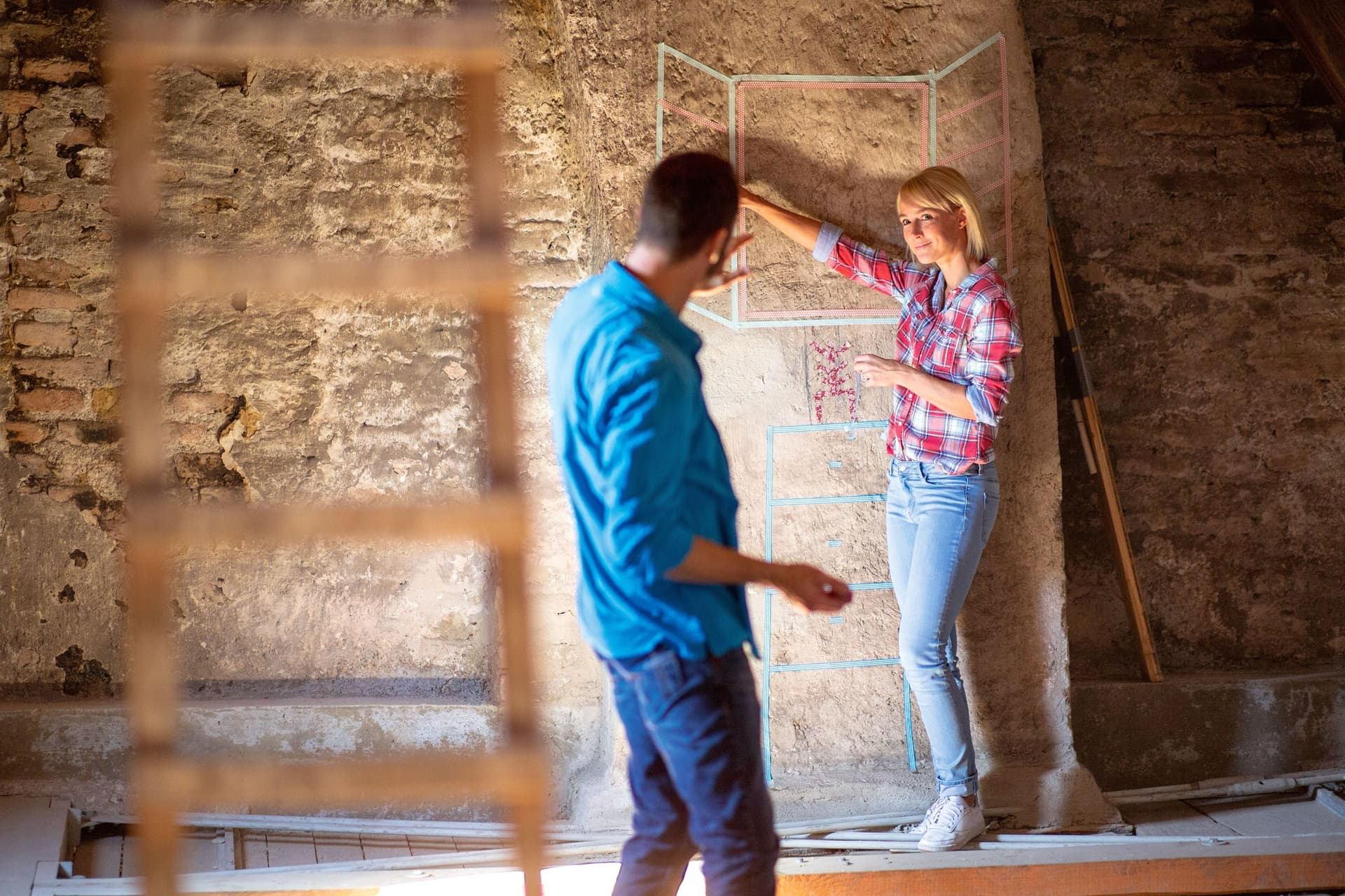 Ein Mann und eine Frau haben auf einer Baustelle mit Krepp-Klebeband ein Fenster an die Wand geklebt.