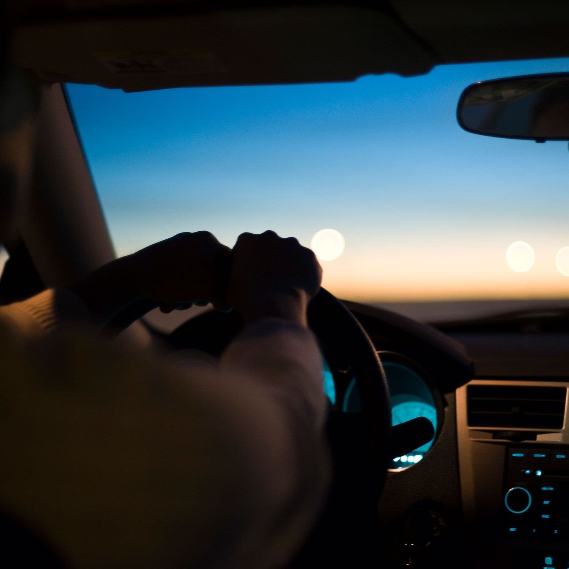 Blick von der Rückbank eines Autos. Man sieht den Fahrer und die Konsole.