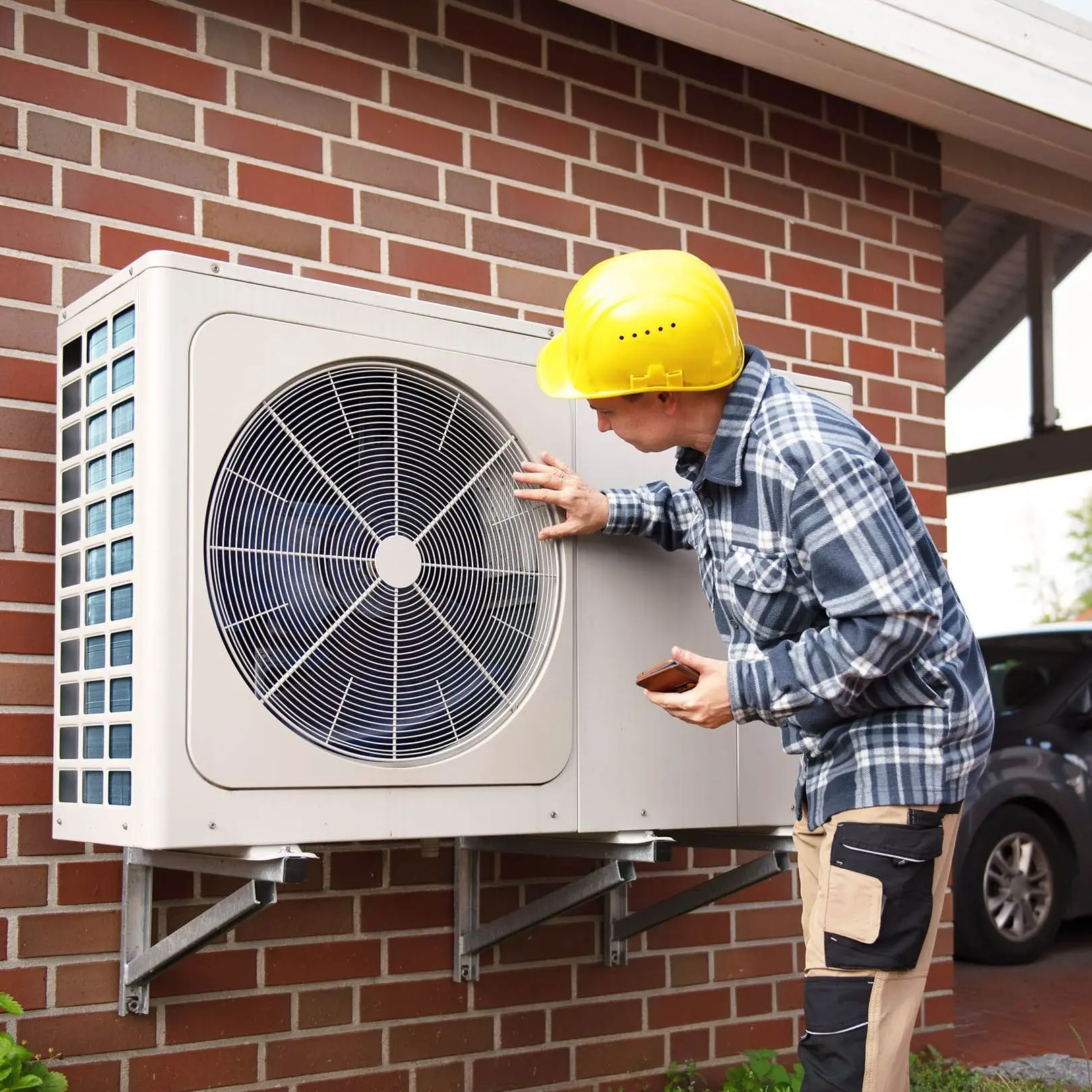 Ein Heizungsbauer in Arbeitskleidung prüft die Funktion einer Luft-Wärmepumpe im Außenbereich eines Hauses.