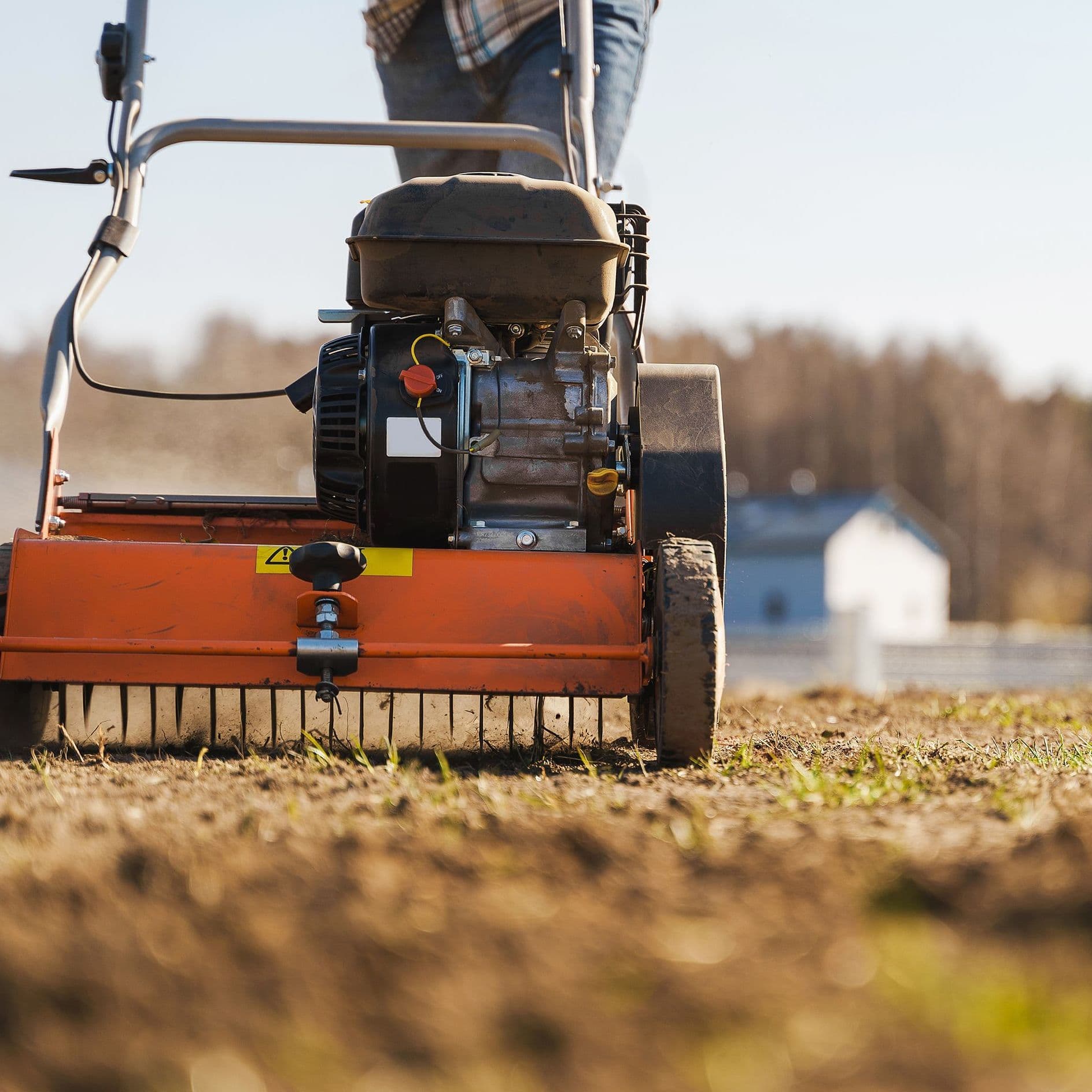 Eine Person bearbeitet den Rasen mit einem Vertikutierer.