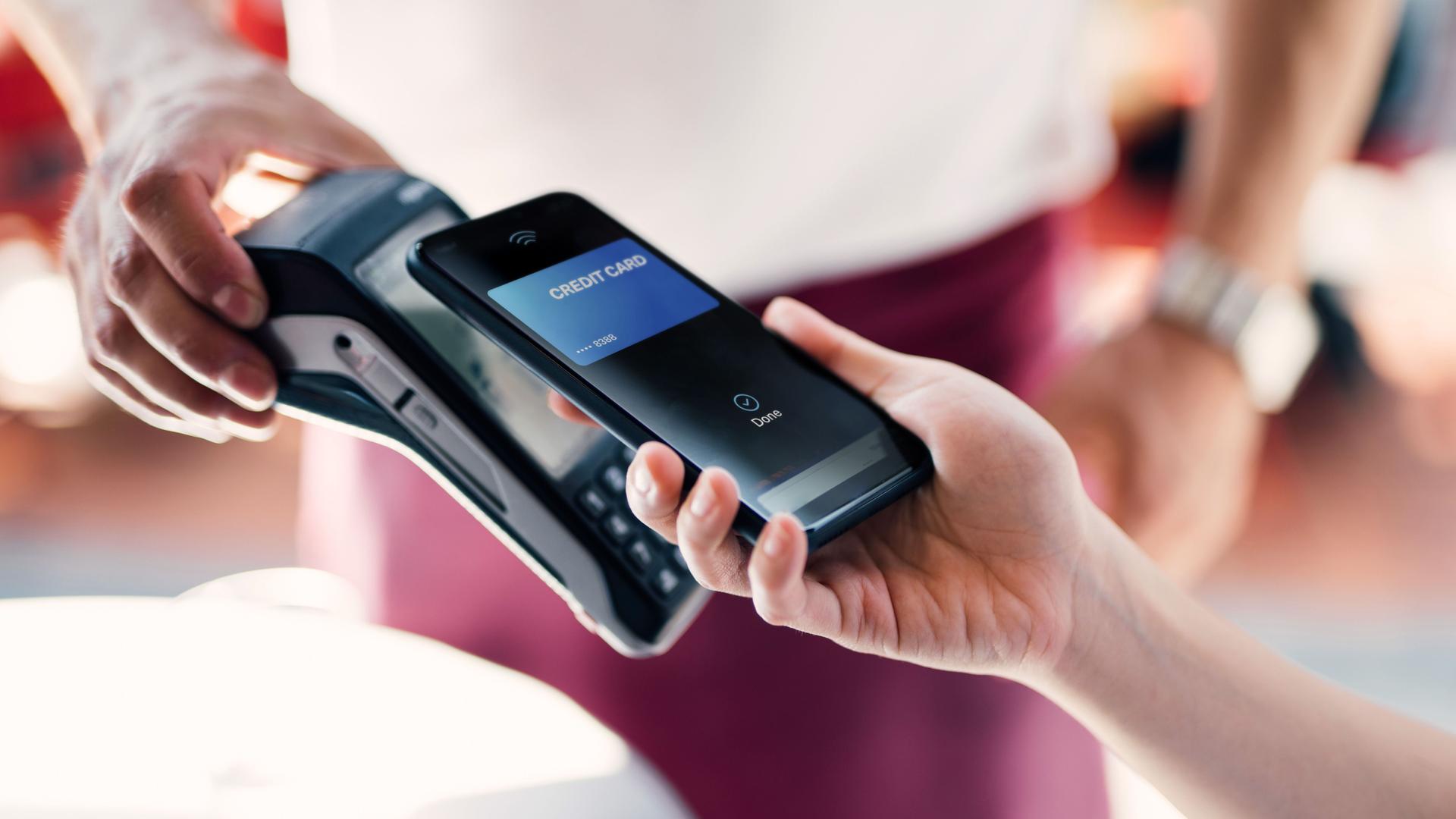 Nahaufnahme einer weiblichen Hand, die ihr Smartphone benutzt, um eine Rechnung im Restaurant bei einem Kellner mit Kartenlesegerät, zu bezahlen.