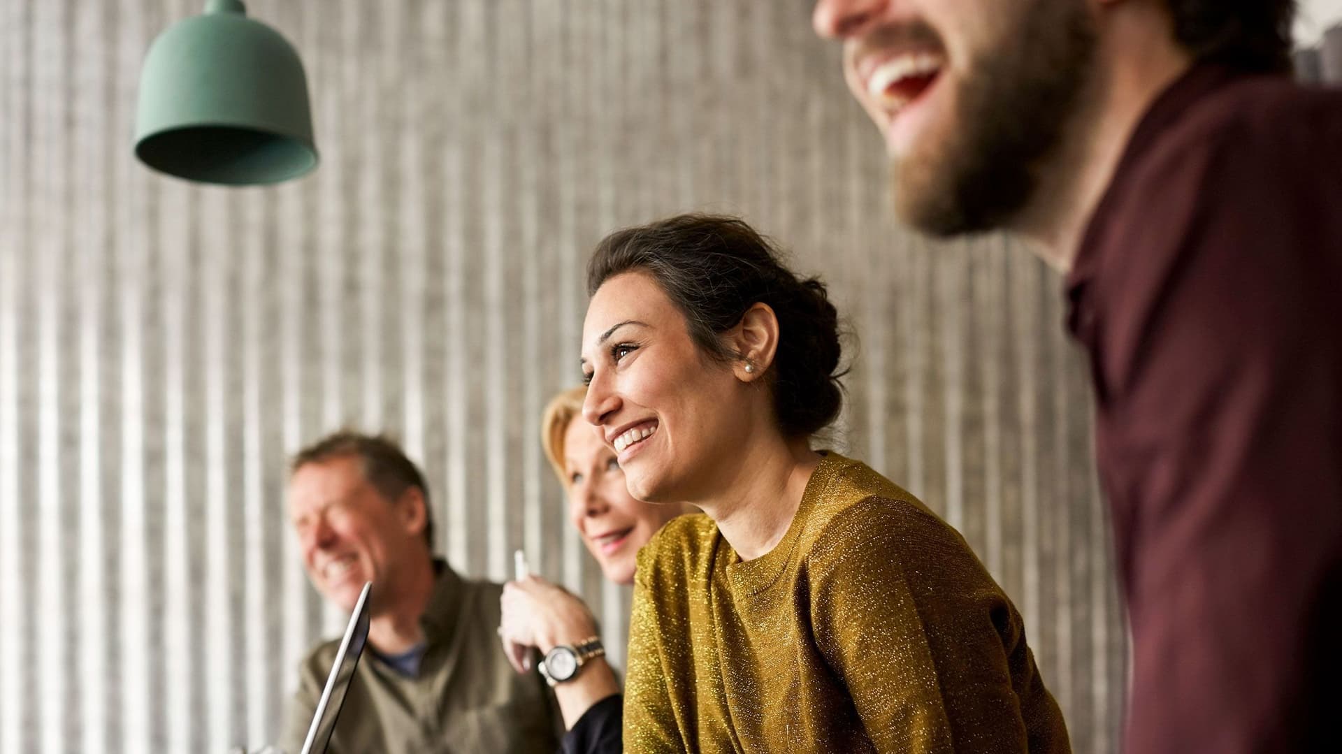 Drei Personen sitzen entspannt in einem Besprechungsraum. Im Vordergrund ist eine junge Frau zu sehen, die freundlich lächelt.