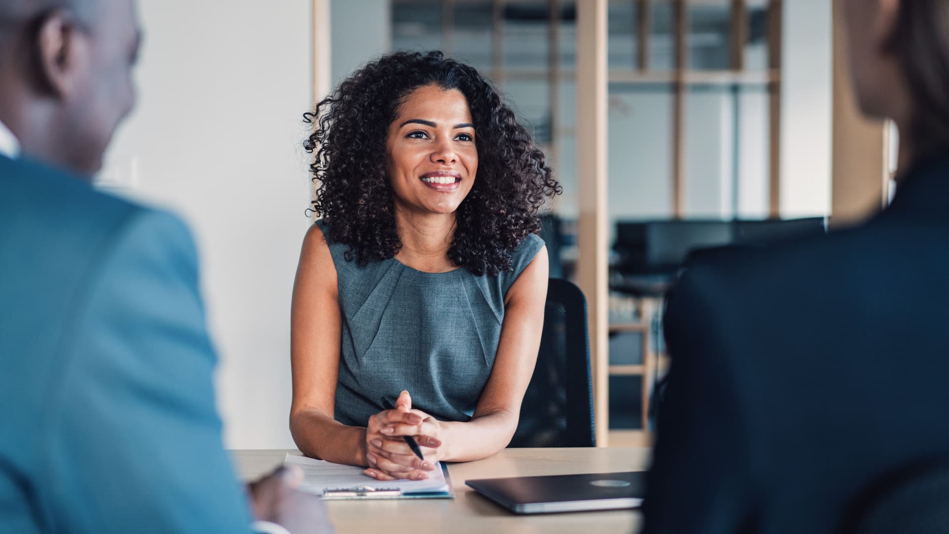 Zwei Frauen und ein Mann sitzen zusammen an einem Tisch in einem Meeting. Auf dem Tisch liegt ein Laptop und Unterlagen.