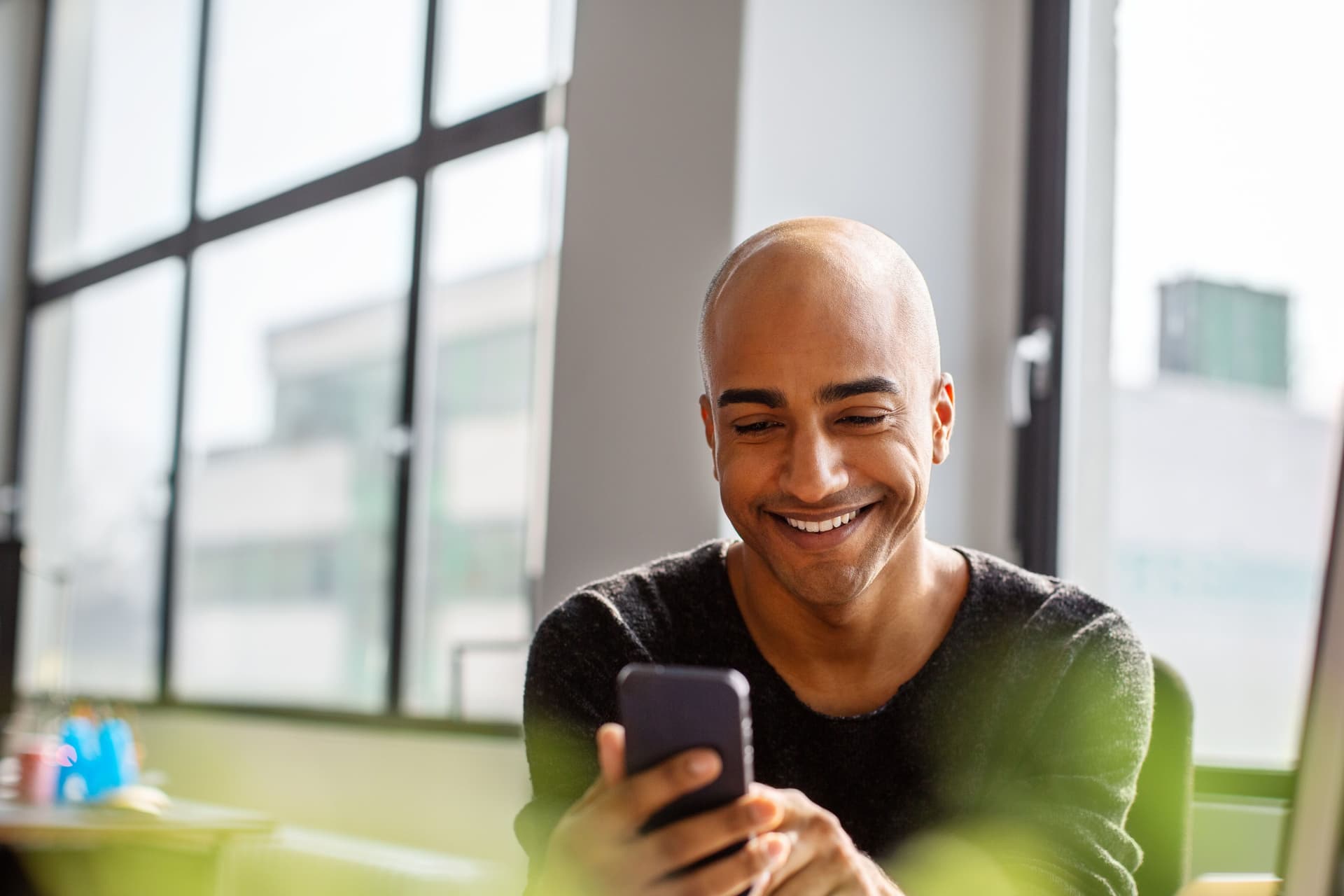 Lächelnder Mann mittleren Alters, der sein Telefon an seinem Schreibtisch benutzt