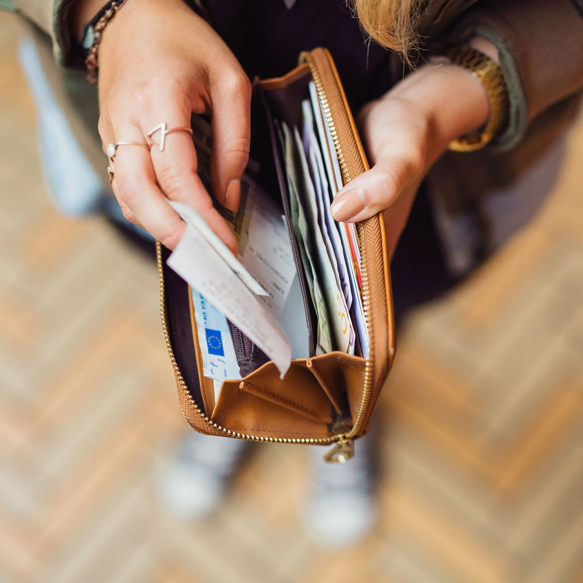 Aufnahme von oben auf die Hände einer Frau, die ein Portemonnaie gefüllt mit Einkaufsbons und Euroscheinen aufhält.