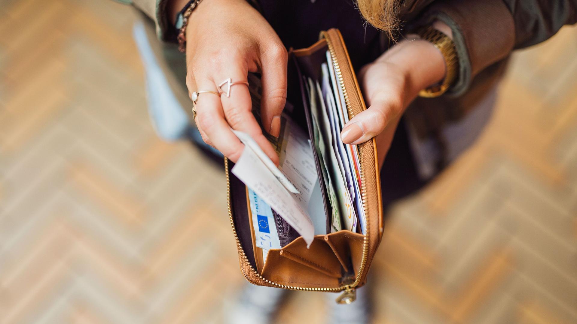 Aufnahme von oben auf die Hände einer Frau, die ein Portemonnaie gefüllt mit Einkaufsbons und Euroscheinen aufhält.