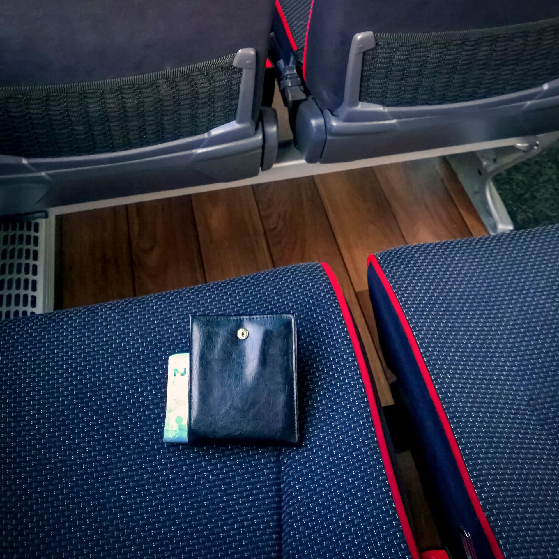 Eine schwarze Brieftasche liegt mit sichtbaren Geldscheinen halb offen auf einem leerem Bussitz.
