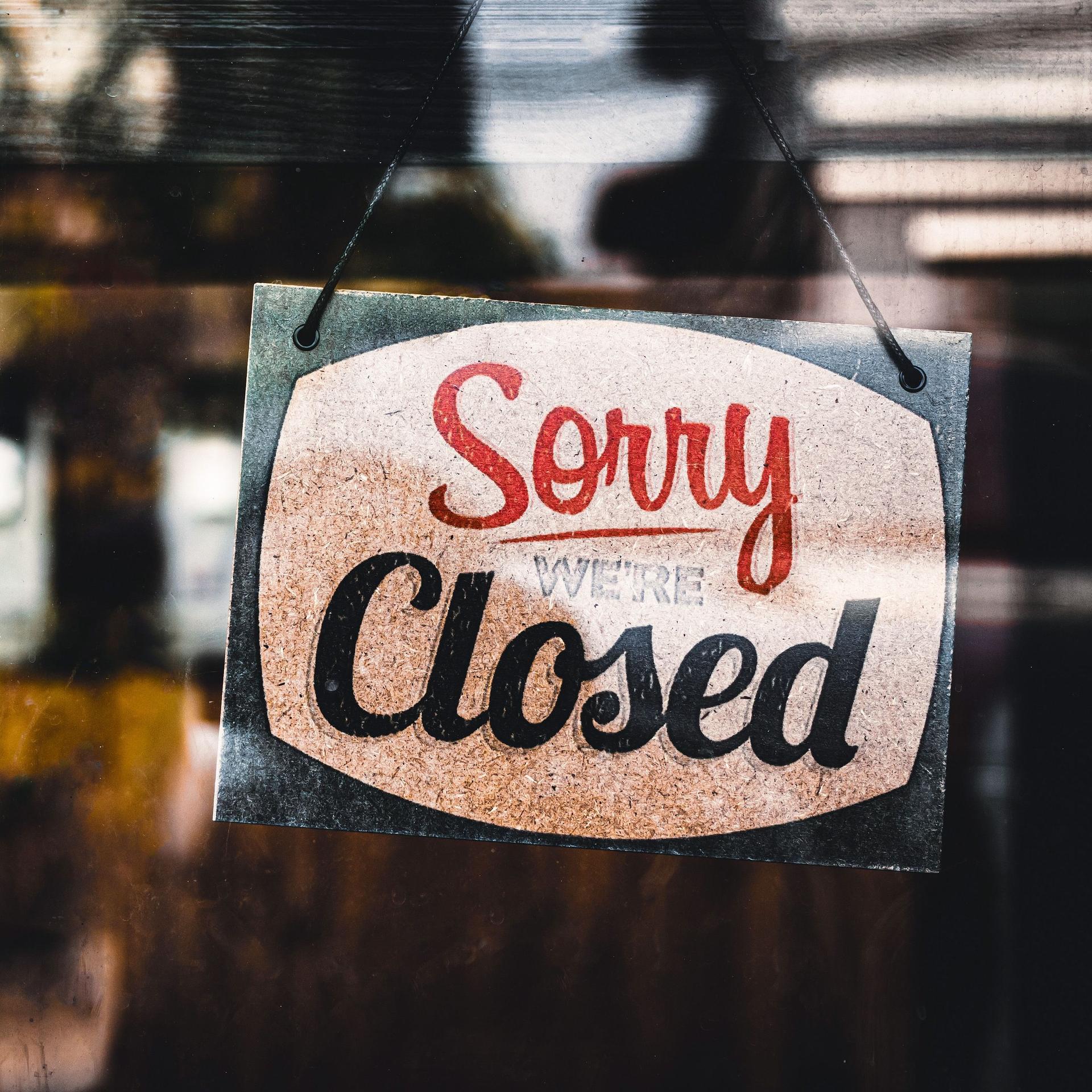 Schild mit der Aufschrift "Sorry we're closed" hängt hinter einer Glasscheibe von einem Laden.