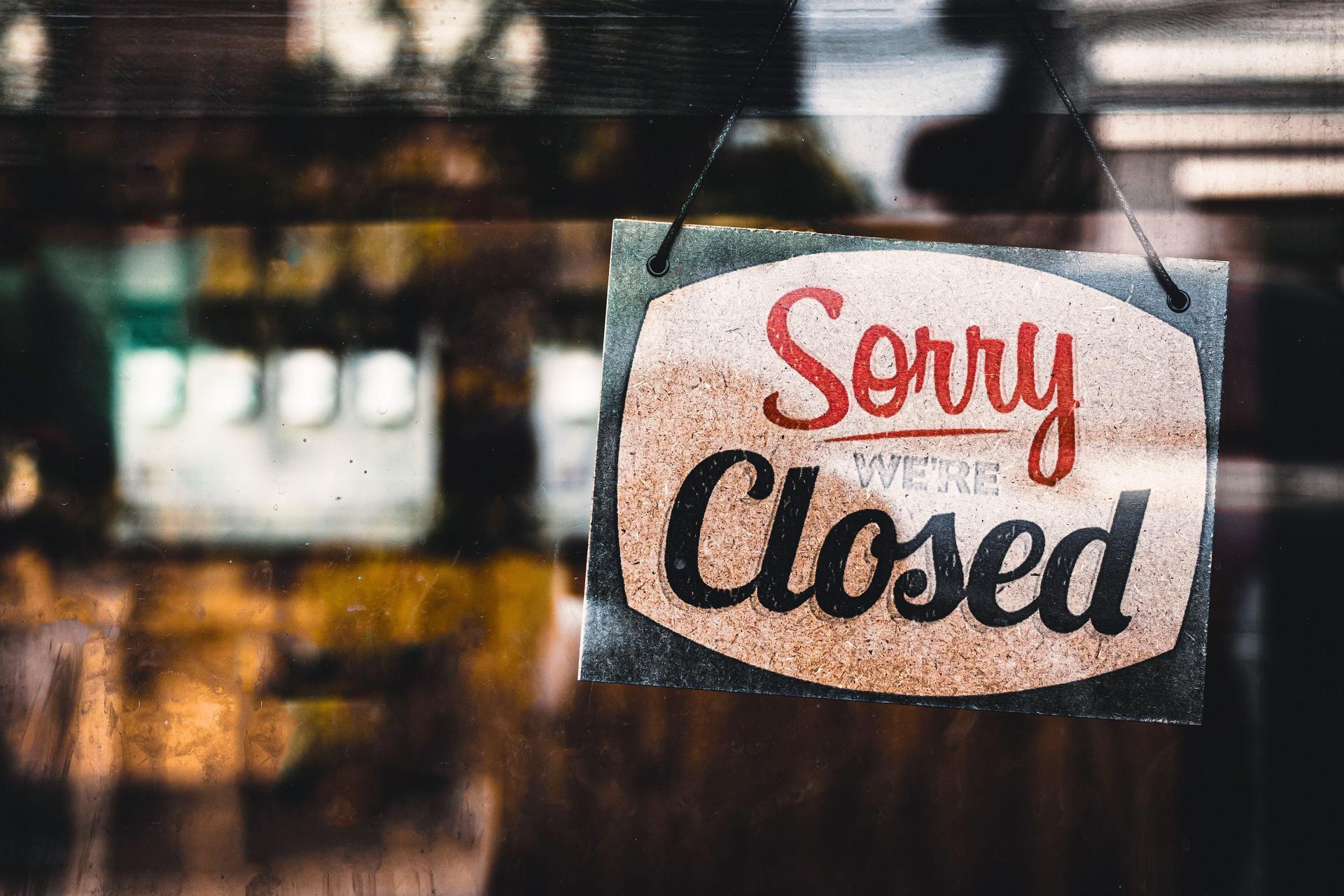 Schild mit der Aufschrift "Sorry we're closed" hängt hinter einer Glasscheibe von einem Laden.