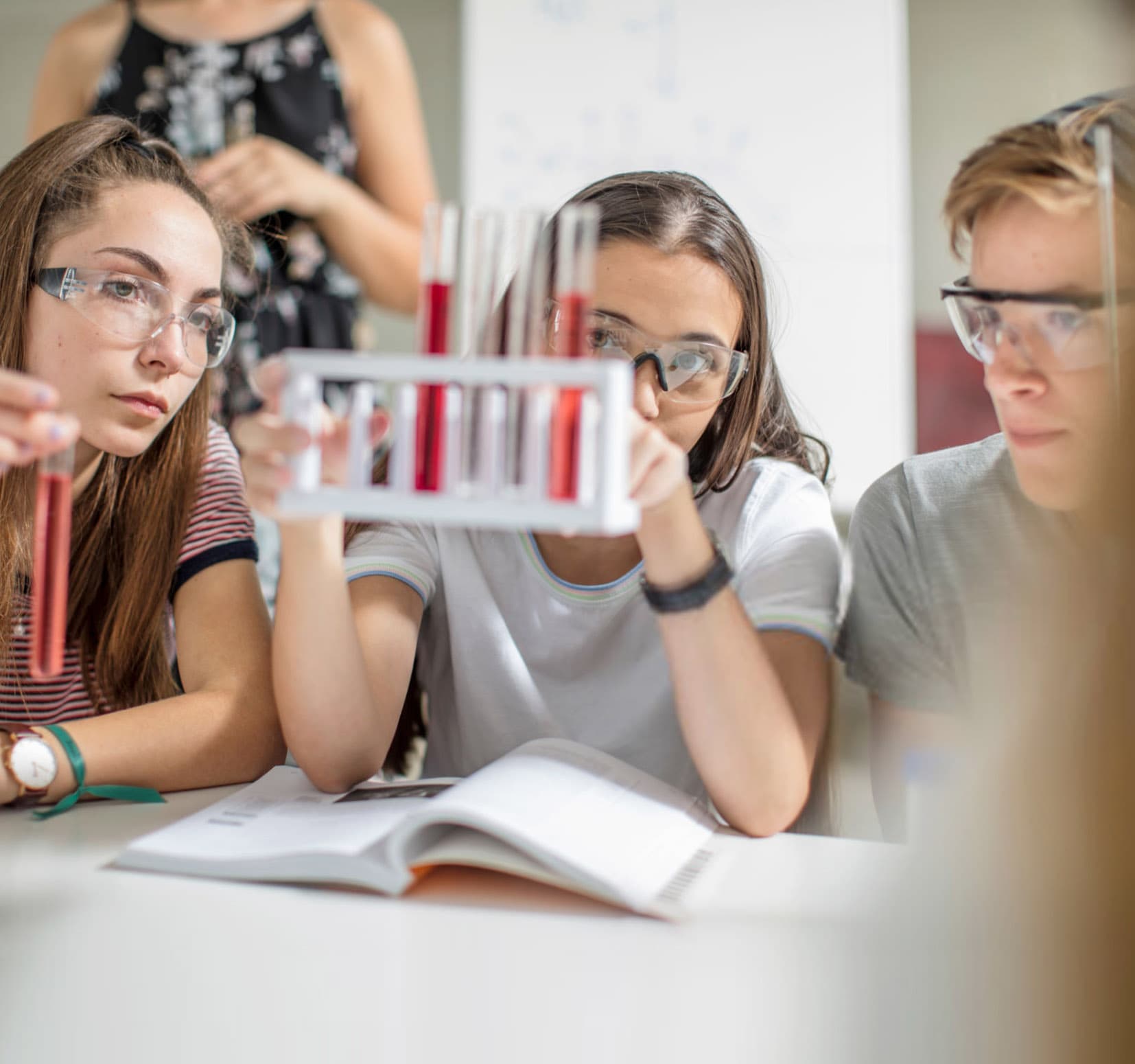 Drei Schülerinnen mit Schutzbrille untersuchen Reagenzgläser im Chemieunterricht