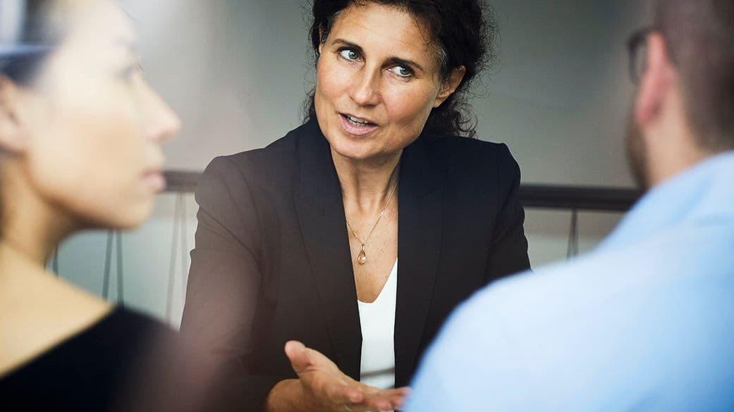 Confident mature female financial advisor discussing with businessman and businesswoman during meeting at office