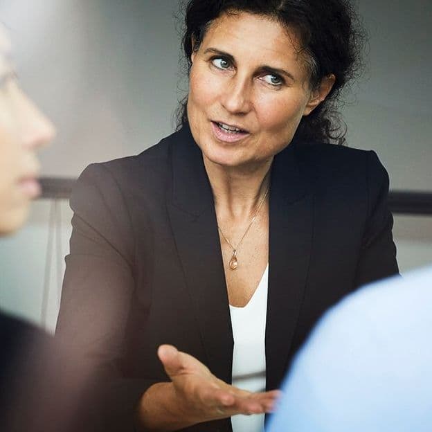 Confident mature female financial advisor discussing with businessman and businesswoman during meeting at office
