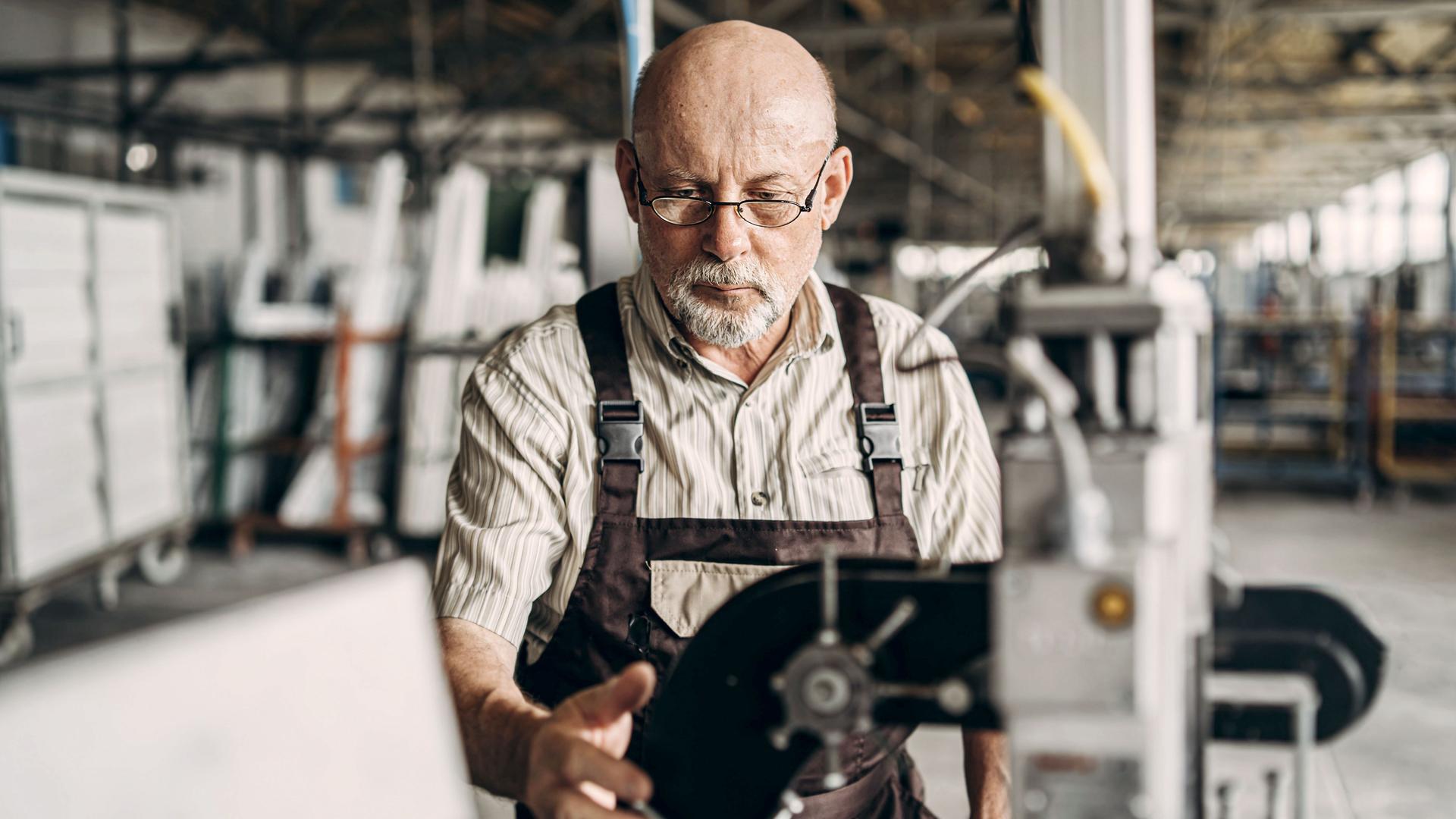 Älterer Mann arbeitet in einer Fabrik konzentriert an einer Maschine.