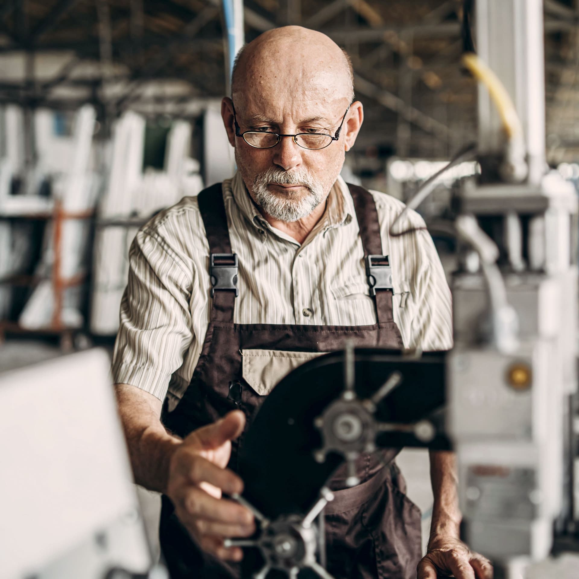 Älterer Mann arbeitet in einer Fabrik konzentriert an einer Maschine.