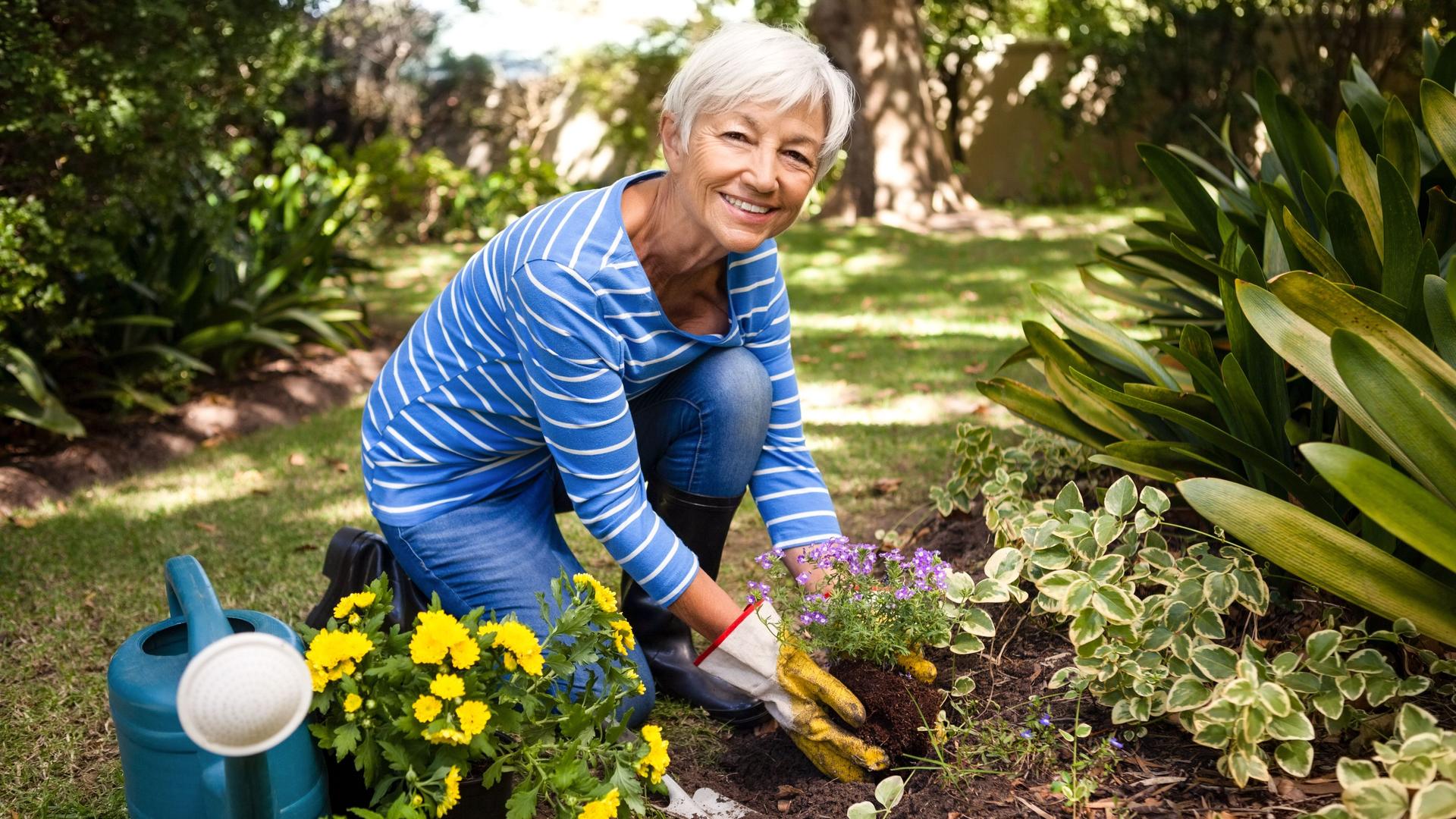 Eine Seniorin arbeitet im Garten und lächelt in die Kamera