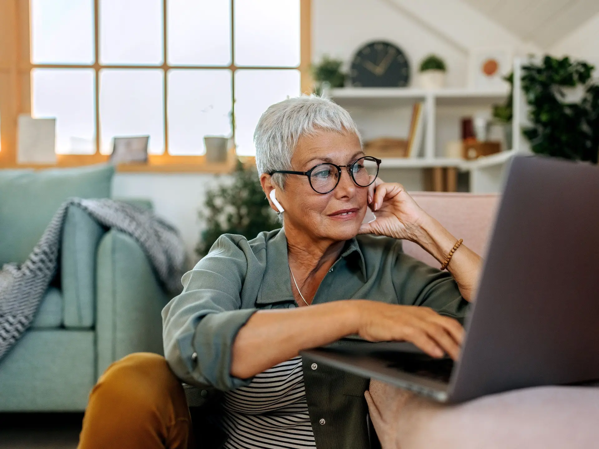 Seniorin sitzt auf den Boden zuhause im Wohnzimmer mit Laptop