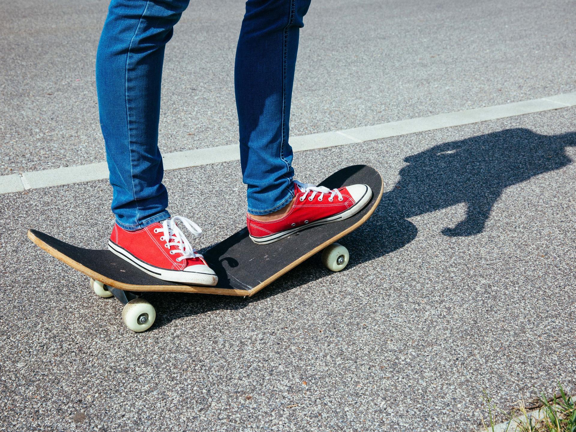 Ein Skateboard bricht während dem Fahren. Die Person darauf trägt rote Turnschuhe und eine enge Jeans.