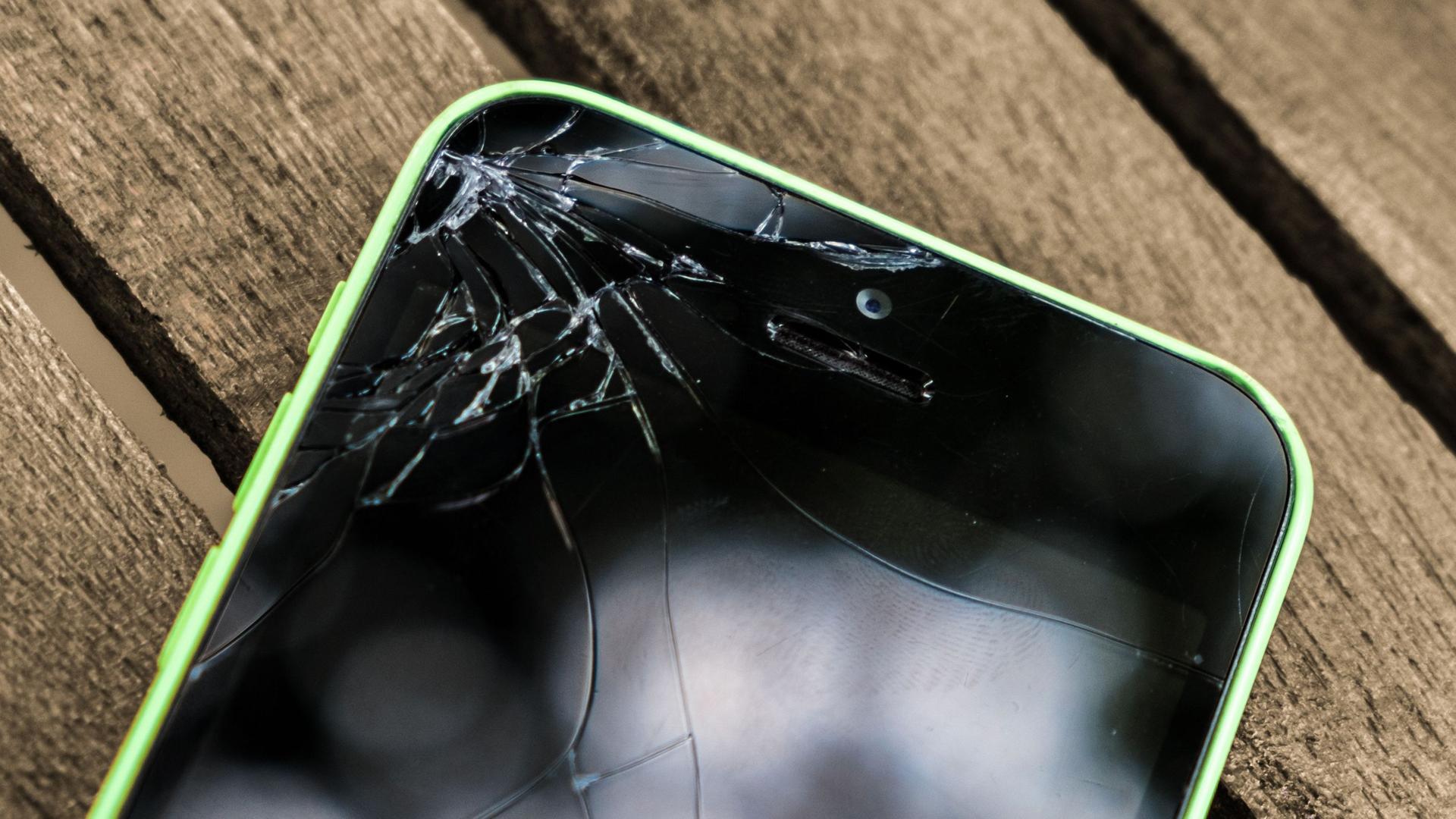 Ein Smartphone mit kaputten Display liegt auf einem Holztisch.
