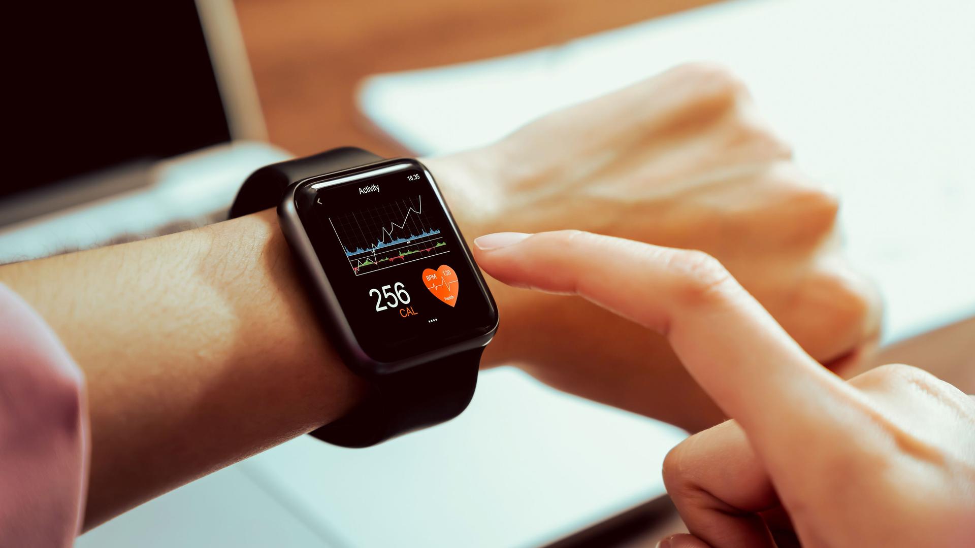 Nahaufnahme einer Hand mit Smartwatch und Gesundheits-App auf dem Bildschirm.