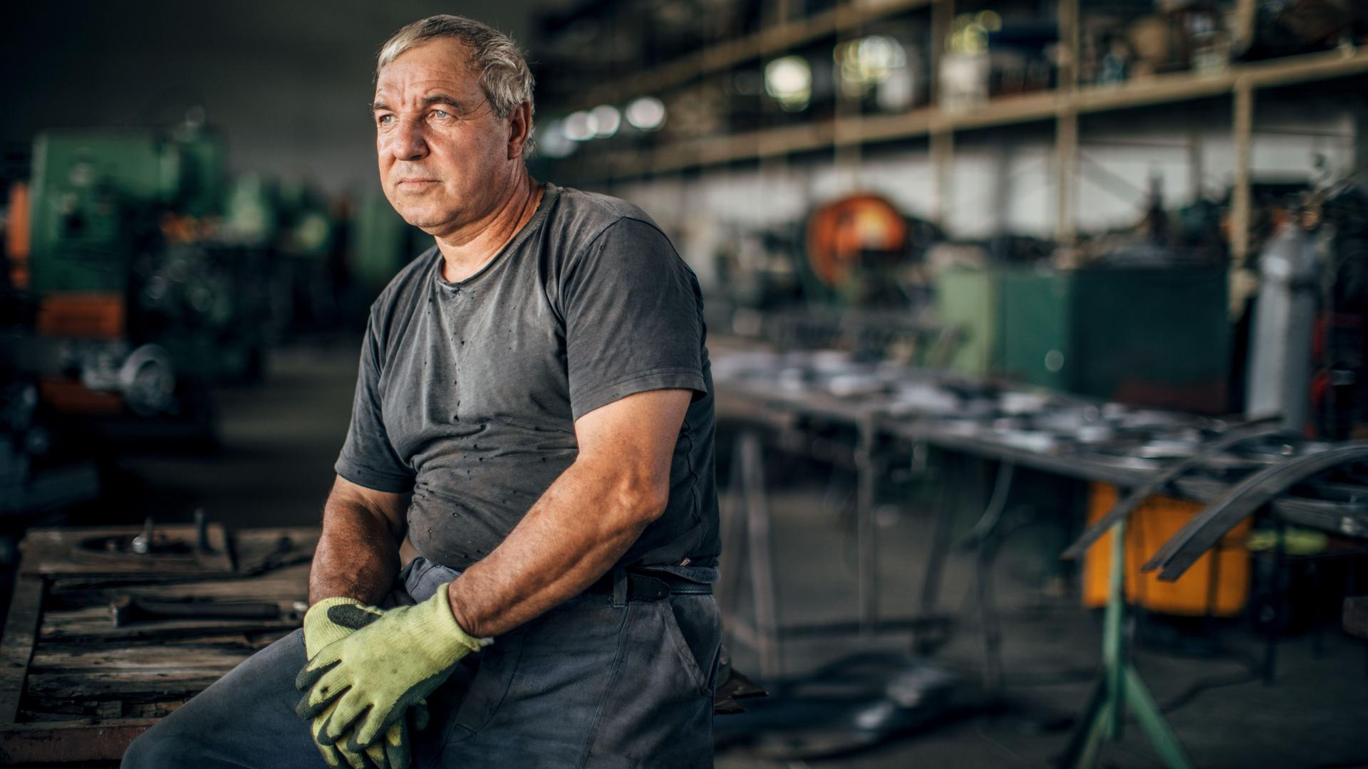 Älterer Mann in Arbeitskleidung in Metallfabrik.