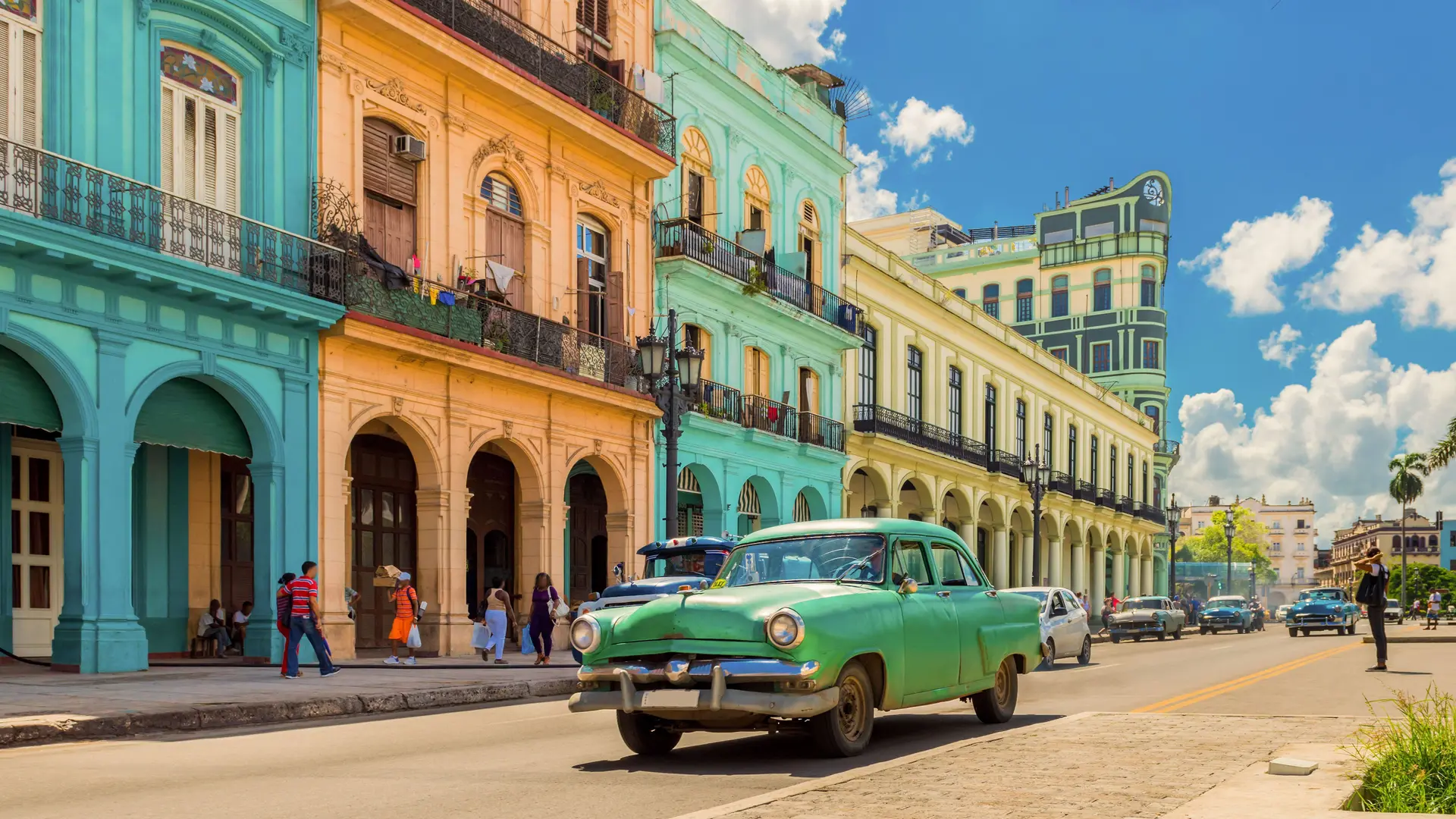 Straßenansicht einer kubanischen Stadt. Ein alter grüner Oldtimer steht auf der Straße.