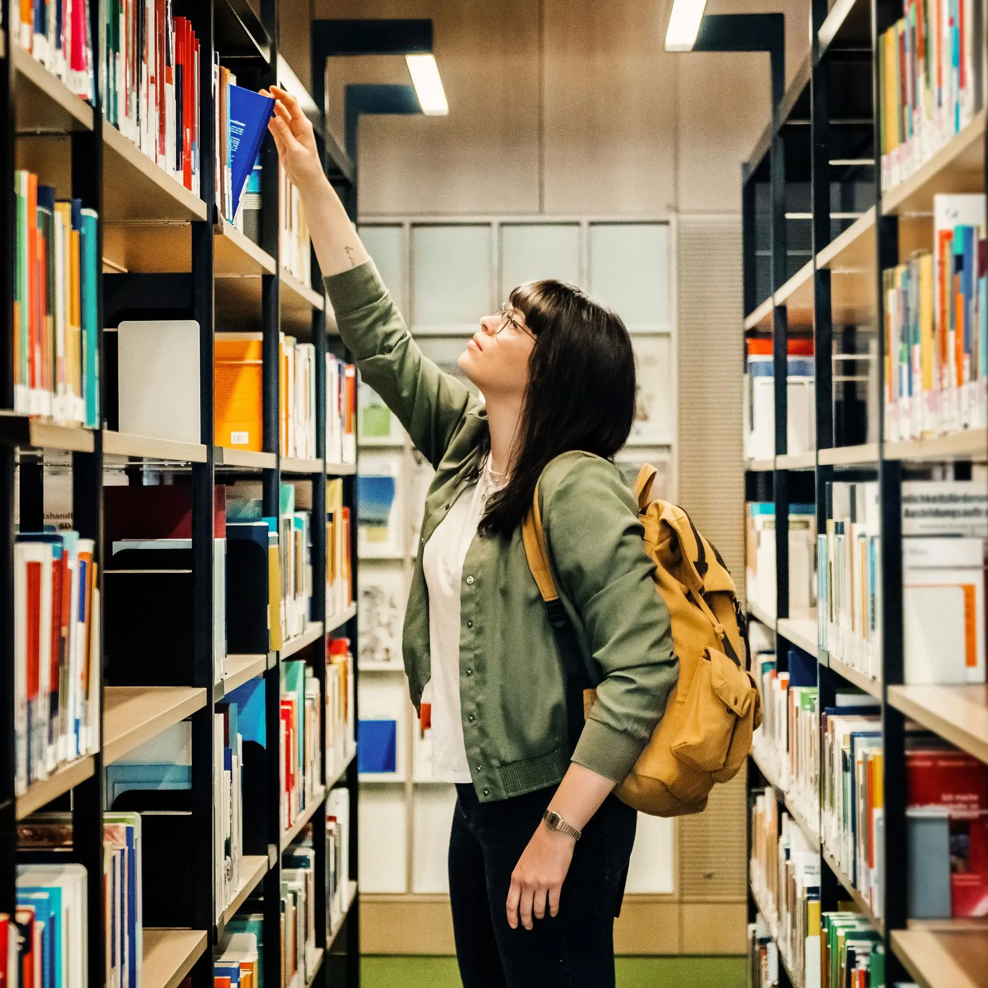 Studentin zieht in Bibliothek ein Buch aus einem Regal