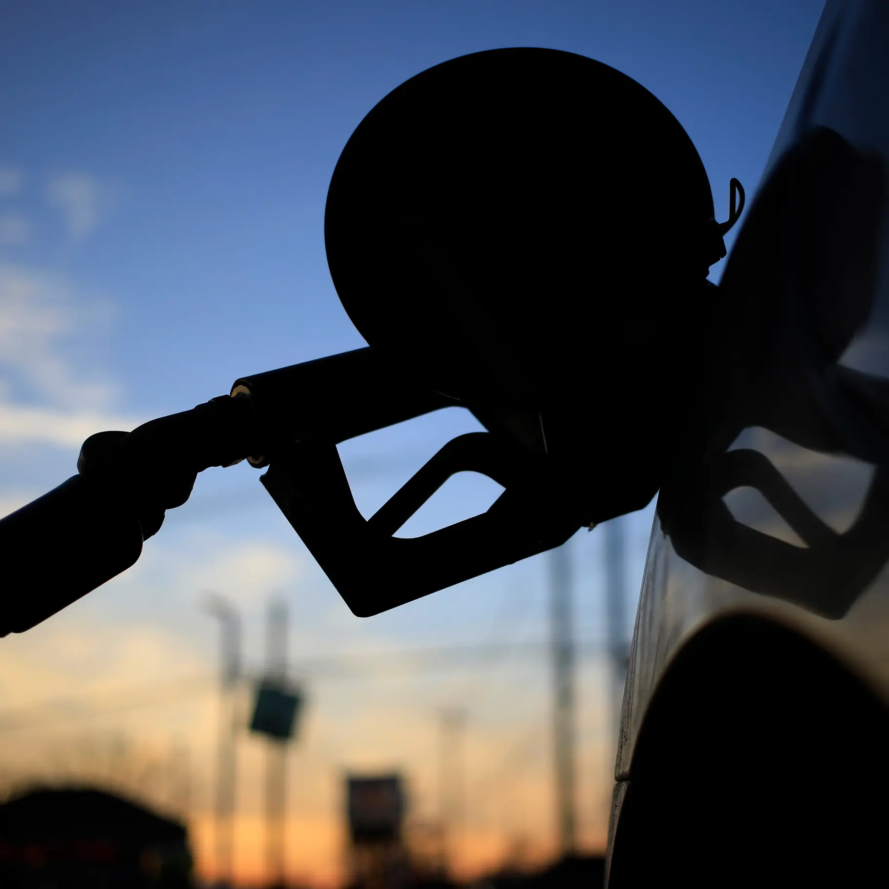 Silhouette eines Tankstützens beim Betanken eines Fahrzeugs im Gegenlicht