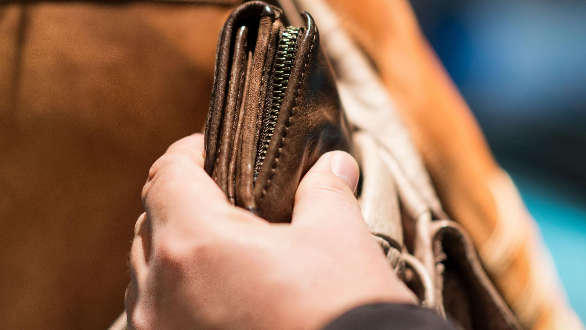 Jemand entwendet ein Portemonnaie aus einer braunen Tasche.