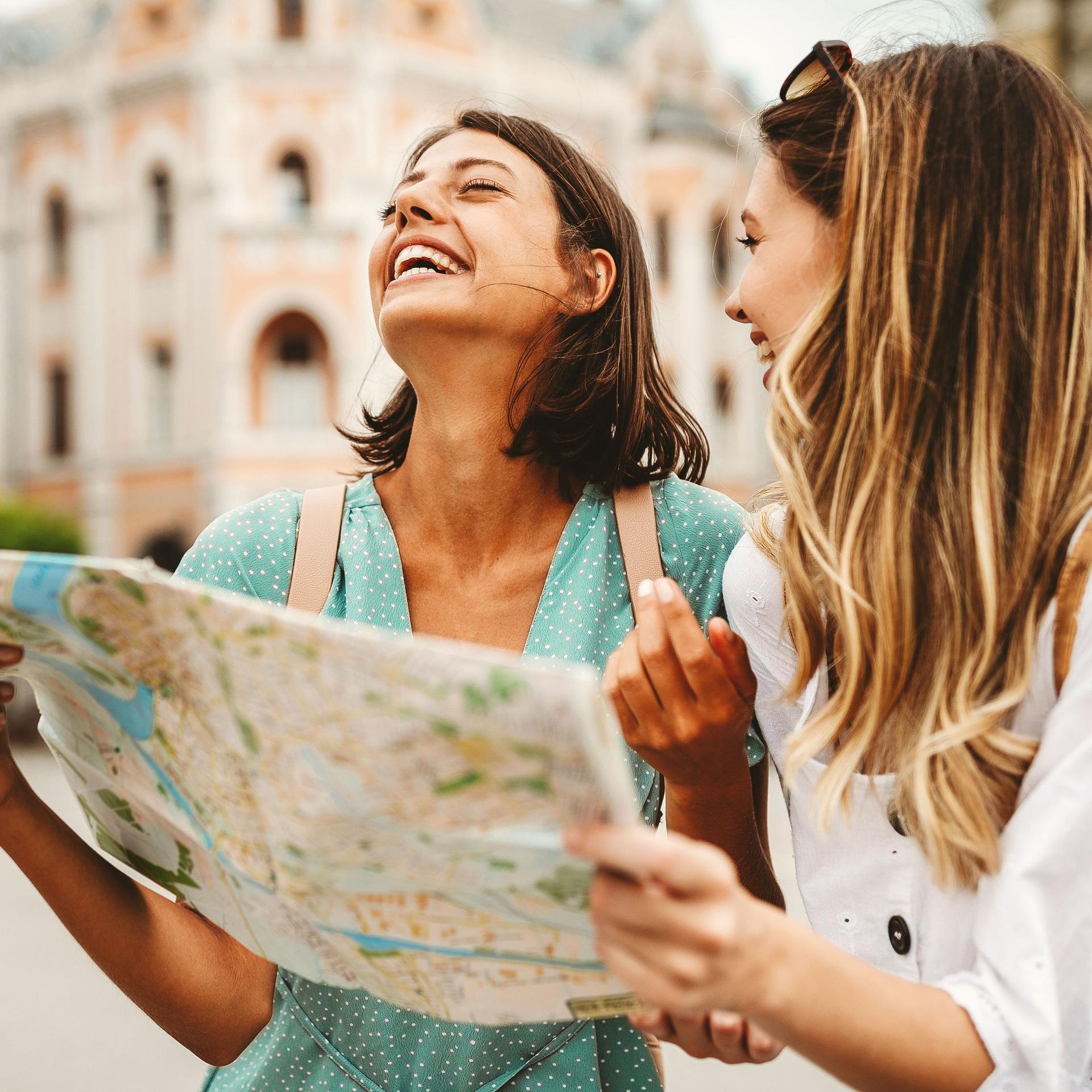 Lachende Touristinnen mit Stadtplan in einer Stadt.