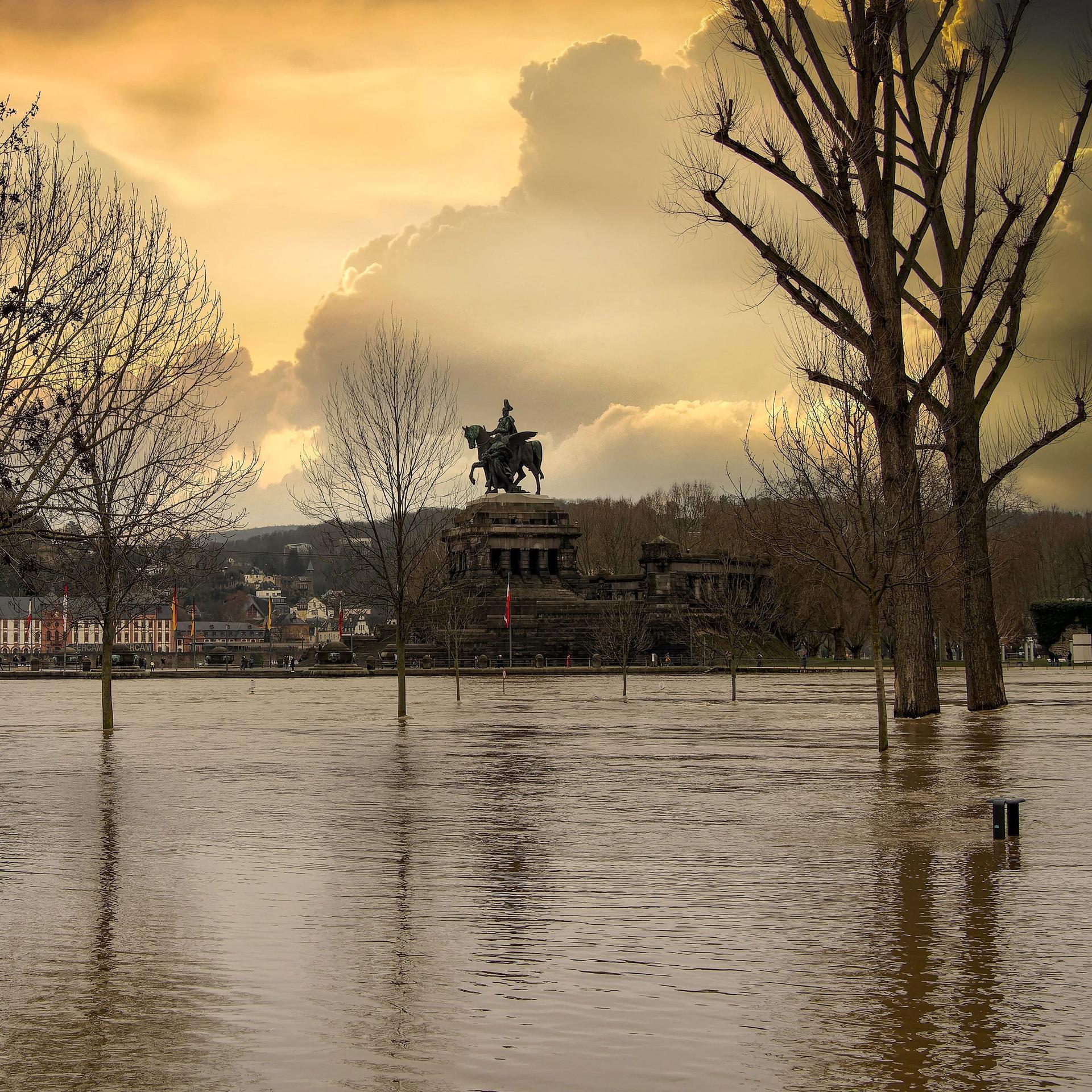 Hochwasser in Koblenz am Deutschen Eck. Im Hintergrund ein dramatischer orangener Himmel mit Wolken,