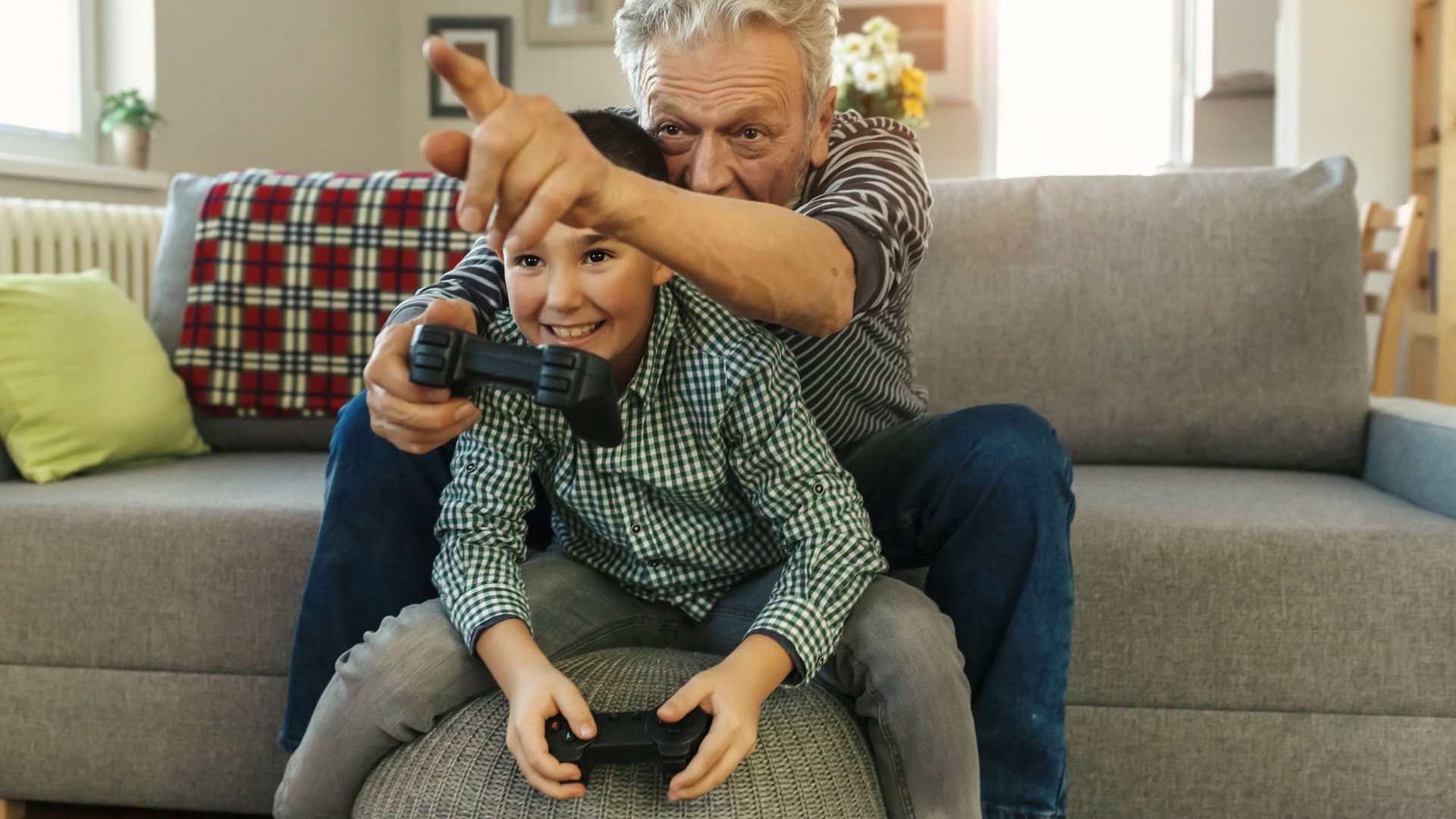 Ein Junge sitzt in den Armen eines Mannes auf der Couch. Sie spielen Konsole
