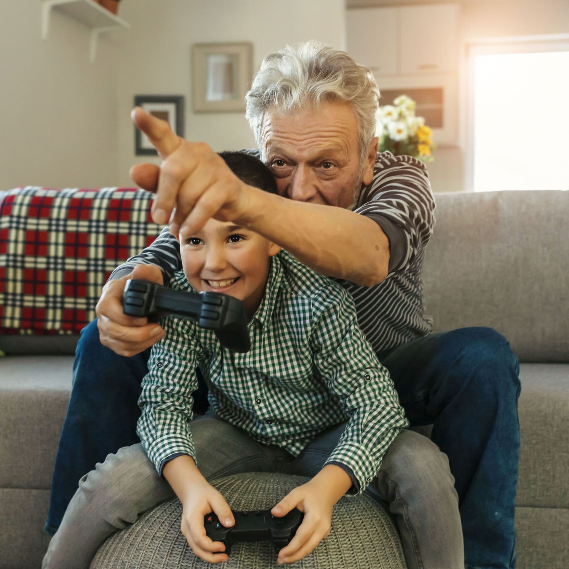 Ein Junge sitzt in den Armen eines Mannes auf der Couch. Sie spielen Konsole