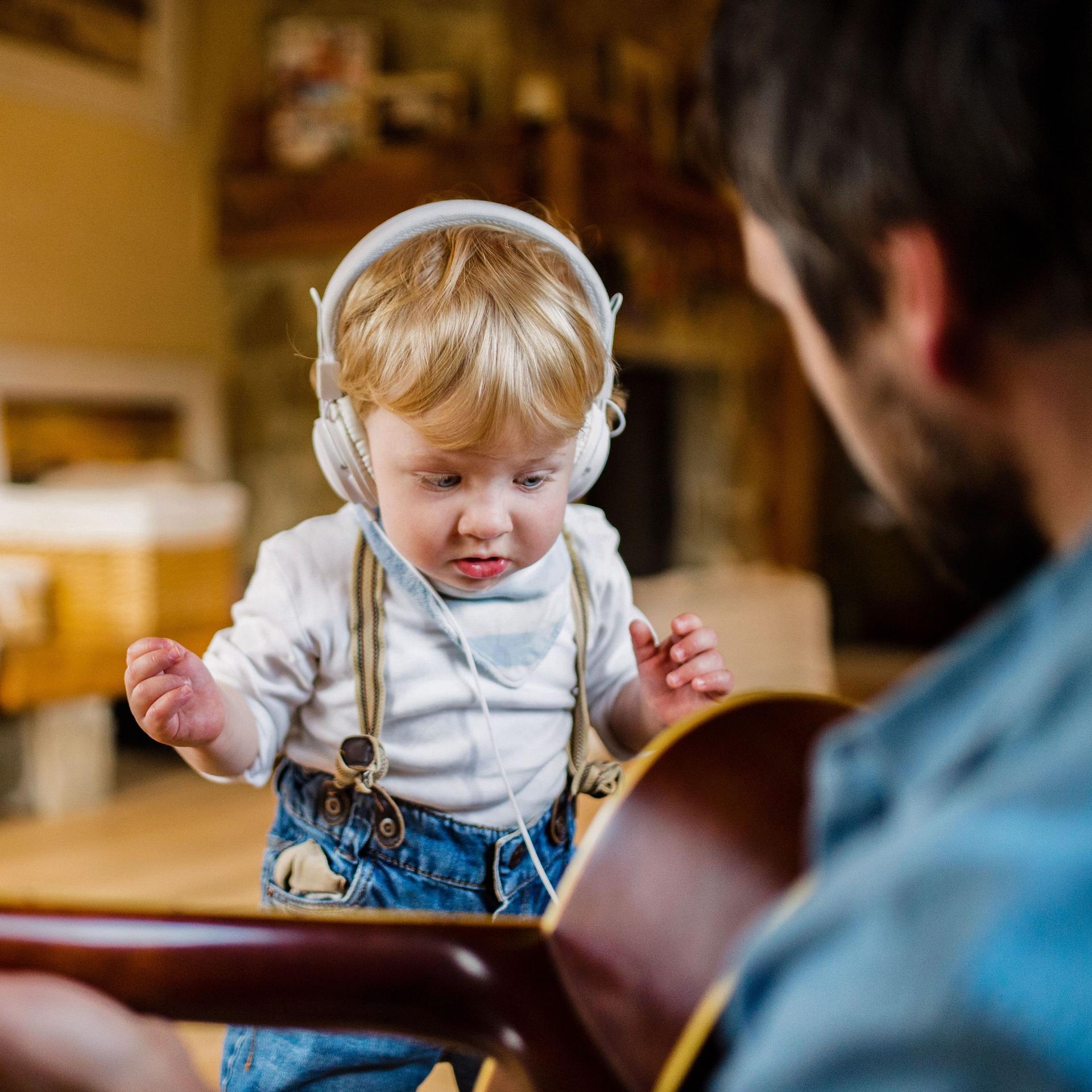 Bild über die Schulter eine Mannes, der Gitarre spielt. Vor ihm steht ein kleiner Junge mit Kopfhörern.