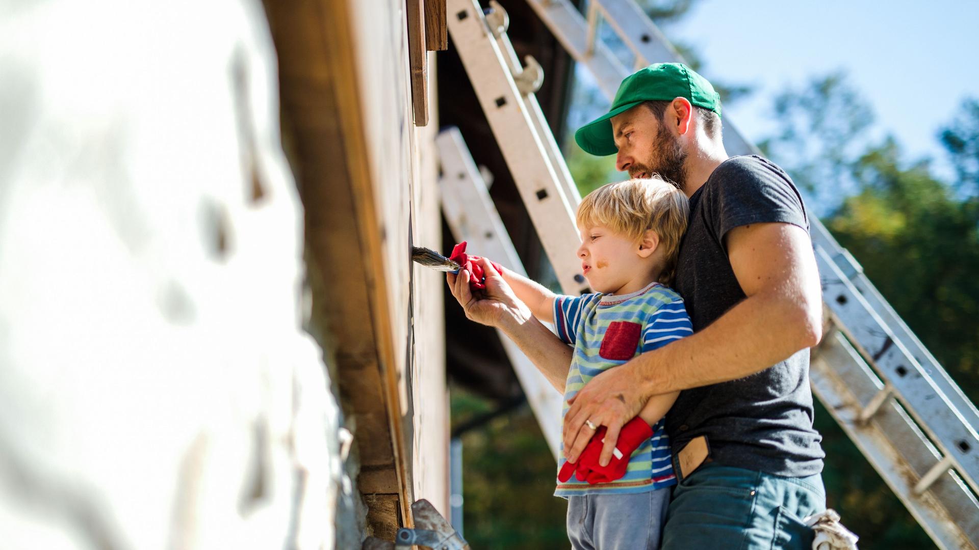 Vater- und Kleinkind streichen einen Holzhaus
