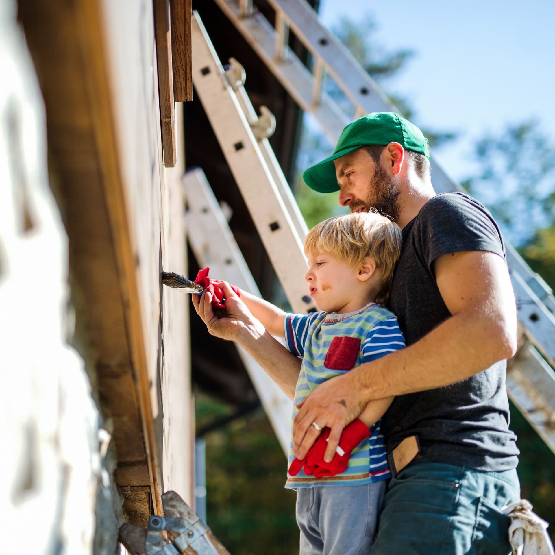 Vater- und Kleinkind streichen einen Holzhaus