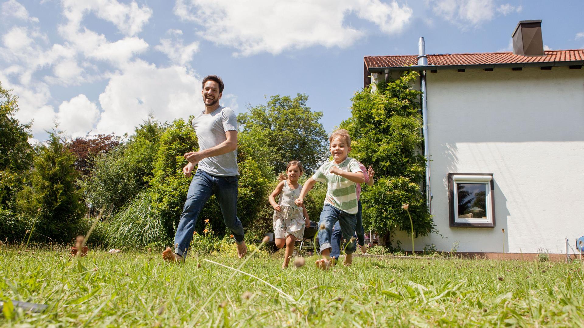 Ein Vater mit Sohn und Tochter rennt im Garten eines Hauses.