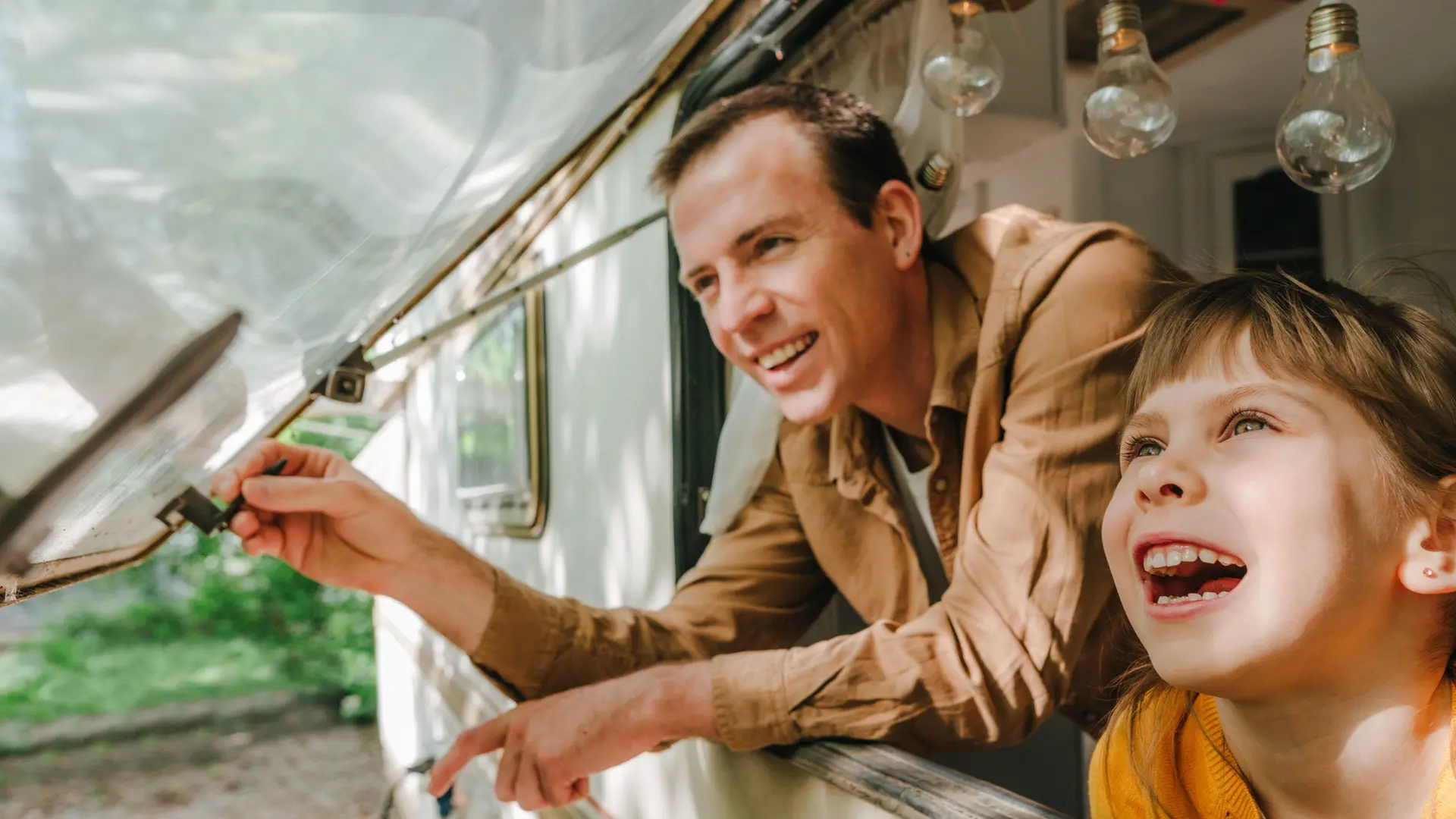 Vater und Tochter blicken lachend aus einem Wohnwagenfenster