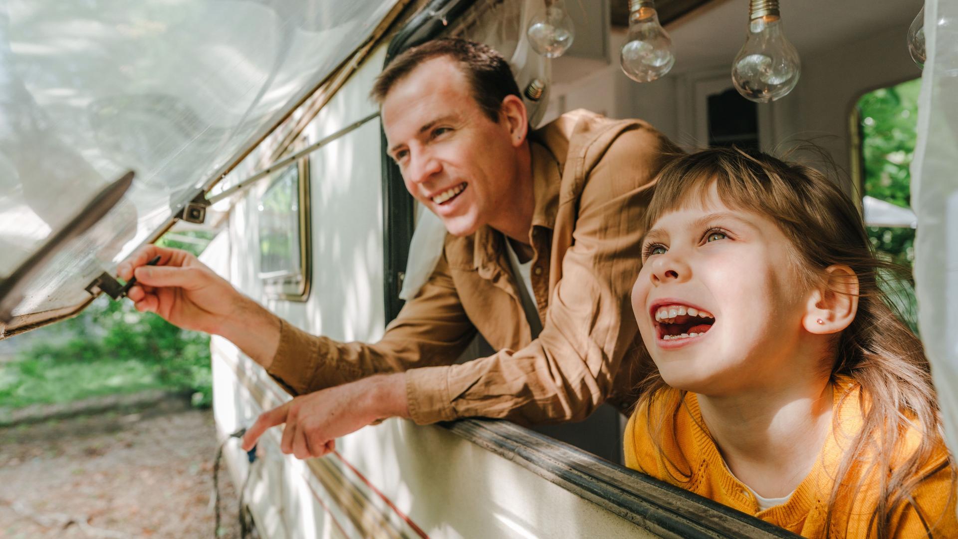 Vater und Tochter blicken lachend aus einem Wohnwagenfenster